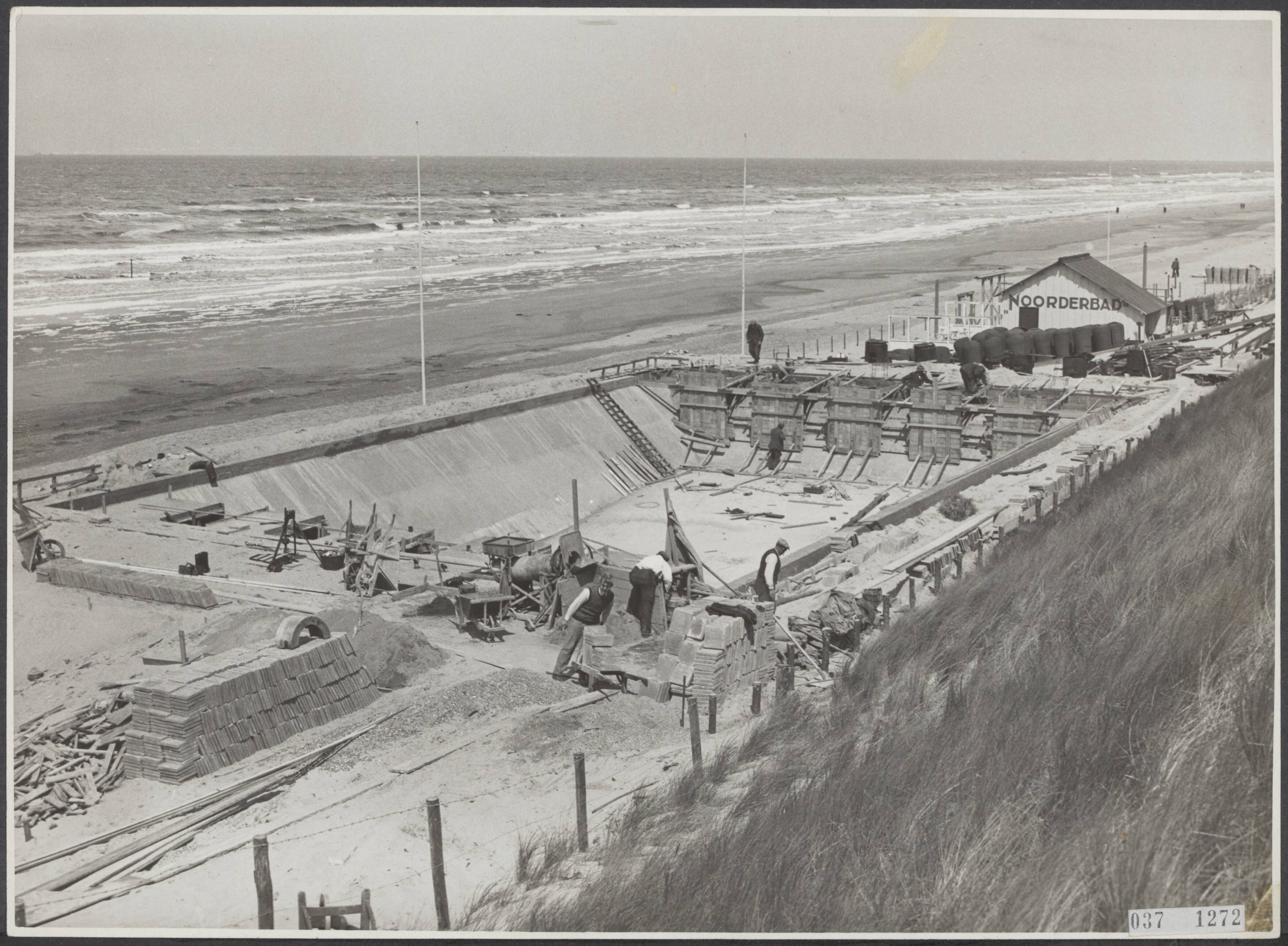 Fotocollectie Elsevier Binnenland — De eigenaar van het "Noorderbad" te Zandvoort is overgegaan tot de bouw van een vast zwembassin op het strand voor het houden van wedstrijden. Het bassin nadert reeds haar voltooiing, het beton storten is bijna beeindigd. Op 25 mei 1933 zal het zwembad officiëel in gebruik genomen worden. — Foto: Fotobureau Stevens / Rechtenvrij. Licentie: Set B: Rechtenvrij / Publiek Domein. Bron: Nationaal Archief. http://hdl.handle.net/10648/adf00874-d0b4-102d-bcf8-003048976d84