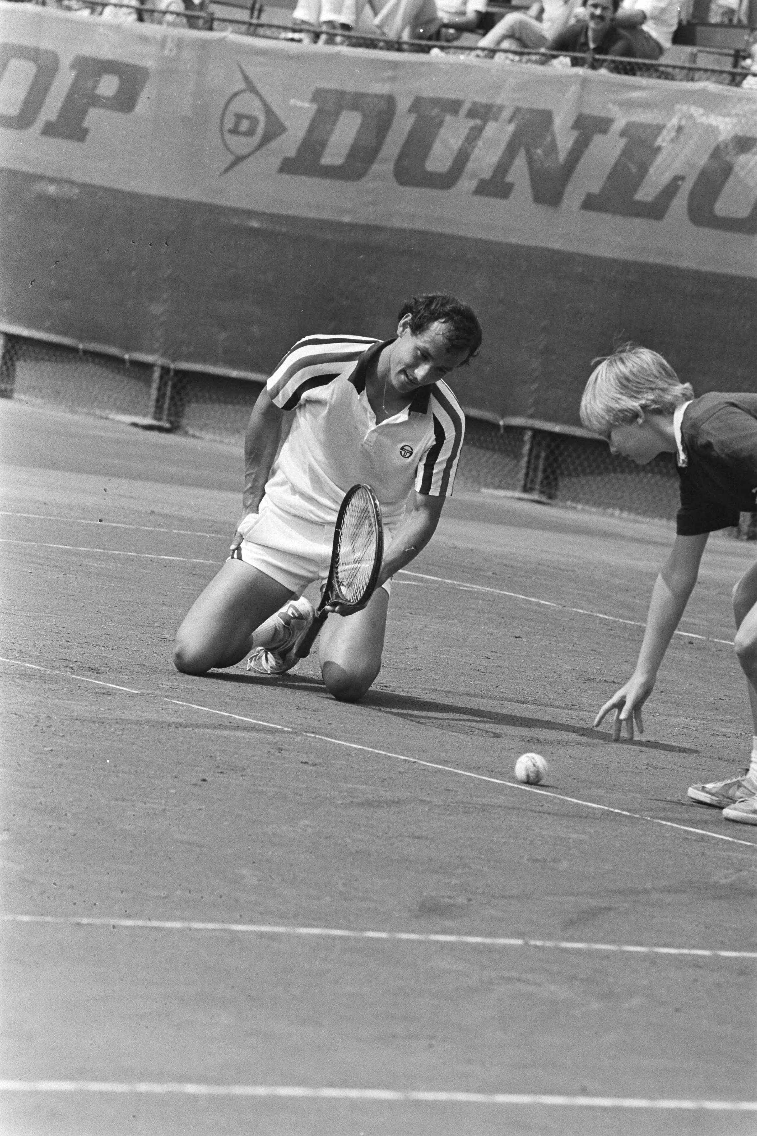 Fotocollectie Anefo — Nationale tenniskampioenschappen, Scheveningen; Sie op zijn knieen — Foto: Bogaerts, Rob / Anefo. Licentie: Set B: Rechtenvrij / Publiek Domein. Bron: Nationaal Archief. http://hdl.handle.net/10648/ad1c62f8-d0b4-102d-bcf8-003048976d84