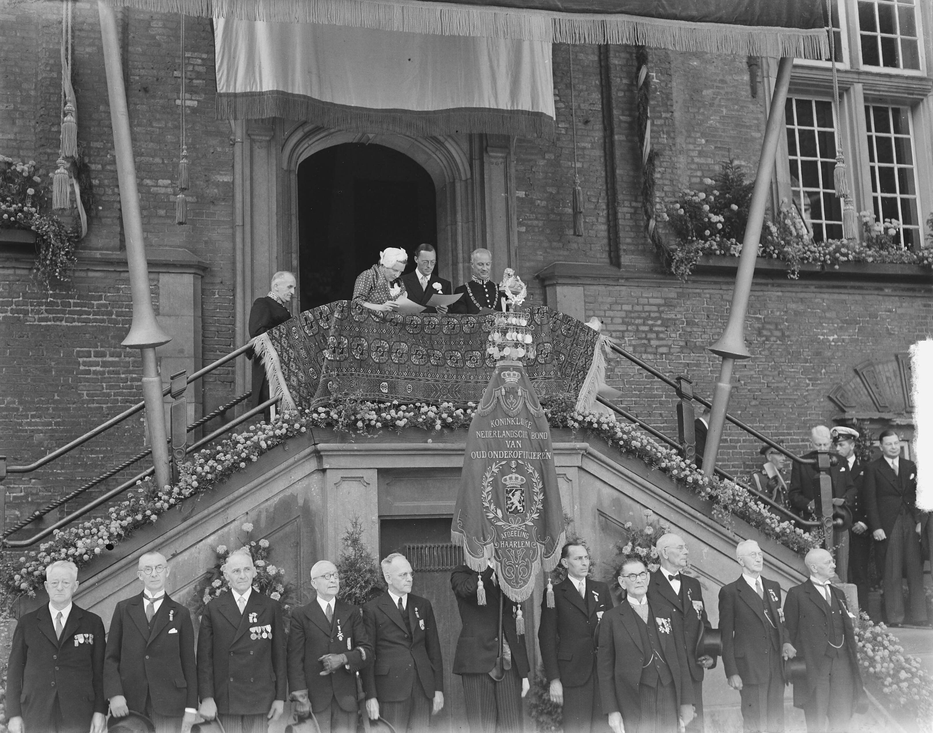 Koningin Juliana en prins Bernhard in Haarlem — Koningin Juliana en prins Bernhard op het bordes van het raadhuis — Foto: Bilsen, Joop van / Anefo. Licentie: Set B: Rechtenvrij / Publiek Domein. Bron: Nationaal Archief. http://hdl.handle.net/10648/a8cb2946-d0b4-102d-bcf8-003048976d84
