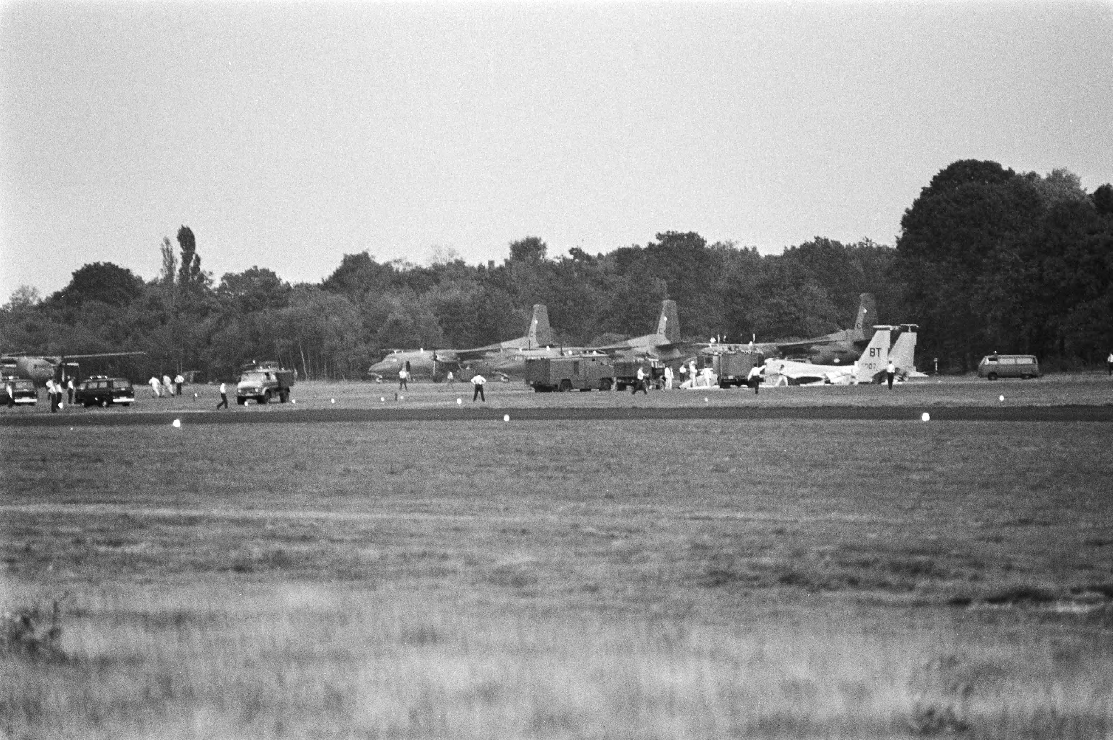 Open dag op luchtmachtbasis Soesterberg — Tijdens een demonstratie op de luchtmachtbasis Soesterberg stortte een McDonnell Douglas F-15 Eagle jacht vliegtuig neer. Hulpdiensten bij het neergestortte vliegtuig. Op de achtergrond geparkeerde Fokker F 27 transportvliegtuigen — Foto: Dijk, Hans van / Anefo. Licentie: Set B: Rechtenvrij / Publiek Domein. Bron: Nationaal Archief. http://hdl.handle.net/10648/ad0396e2-d0b4-102d-bcf8-003048976d84