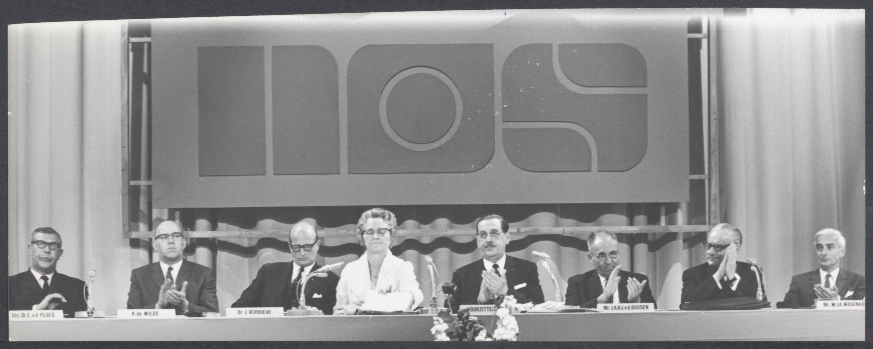 NOS. en NTS - Nederland — De minister van Cultuur, Recreatie en Maatschappelijk Werk heeft het nieuwe bestuur van de Nederlandse Omroep Stichting officieel geinstalleerd. Het bestuur achter de tafel. Op de achtergrond de letters N.O.S. — Foto: Verhoeff, Bert / Anefo. Licentie: Set B: Rechtenvrij / Publiek Domein. Bron: Nationaal Archief. http://hdl.handle.net/10648/9501e478-aefa-cd24-57e8-db240b1837bc