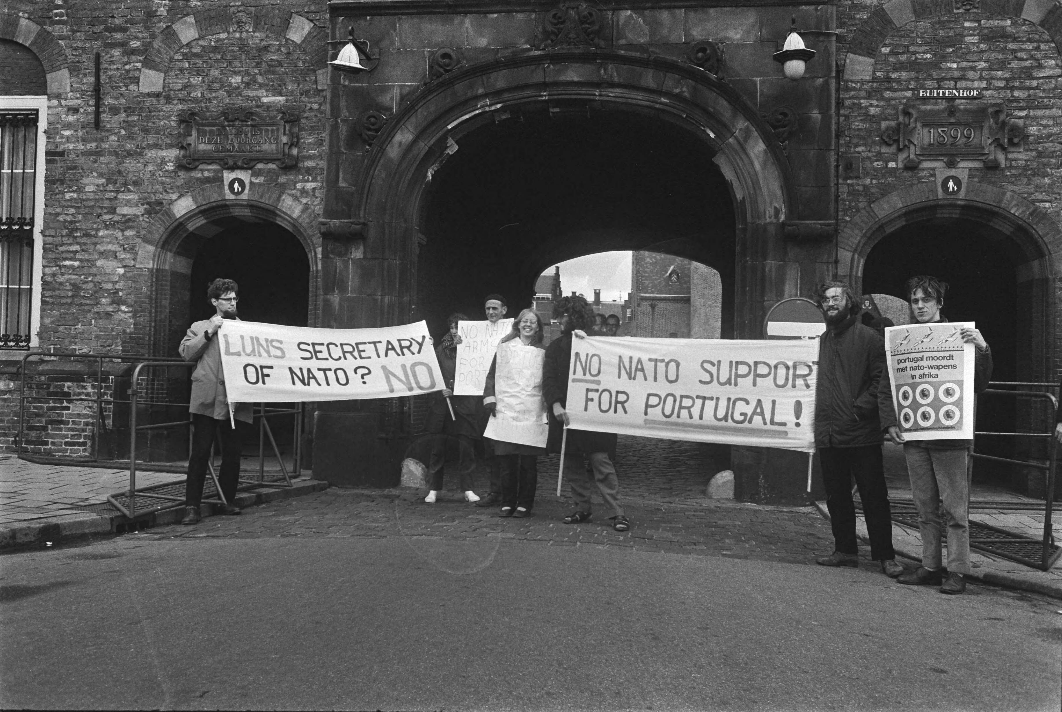 Fotocollectie Anefo — Demonstranten met borden tegen NATO-vergadering voor toegangspoort Binnenhof Den Haag — Foto: Koch, Eric / Anefo. Licentie: Set B: Rechtenvrij / Publiek Domein. Bron: Nationaal Archief. http://hdl.handle.net/10648/aba978b6-d0b4-102d-bcf8-003048976d84