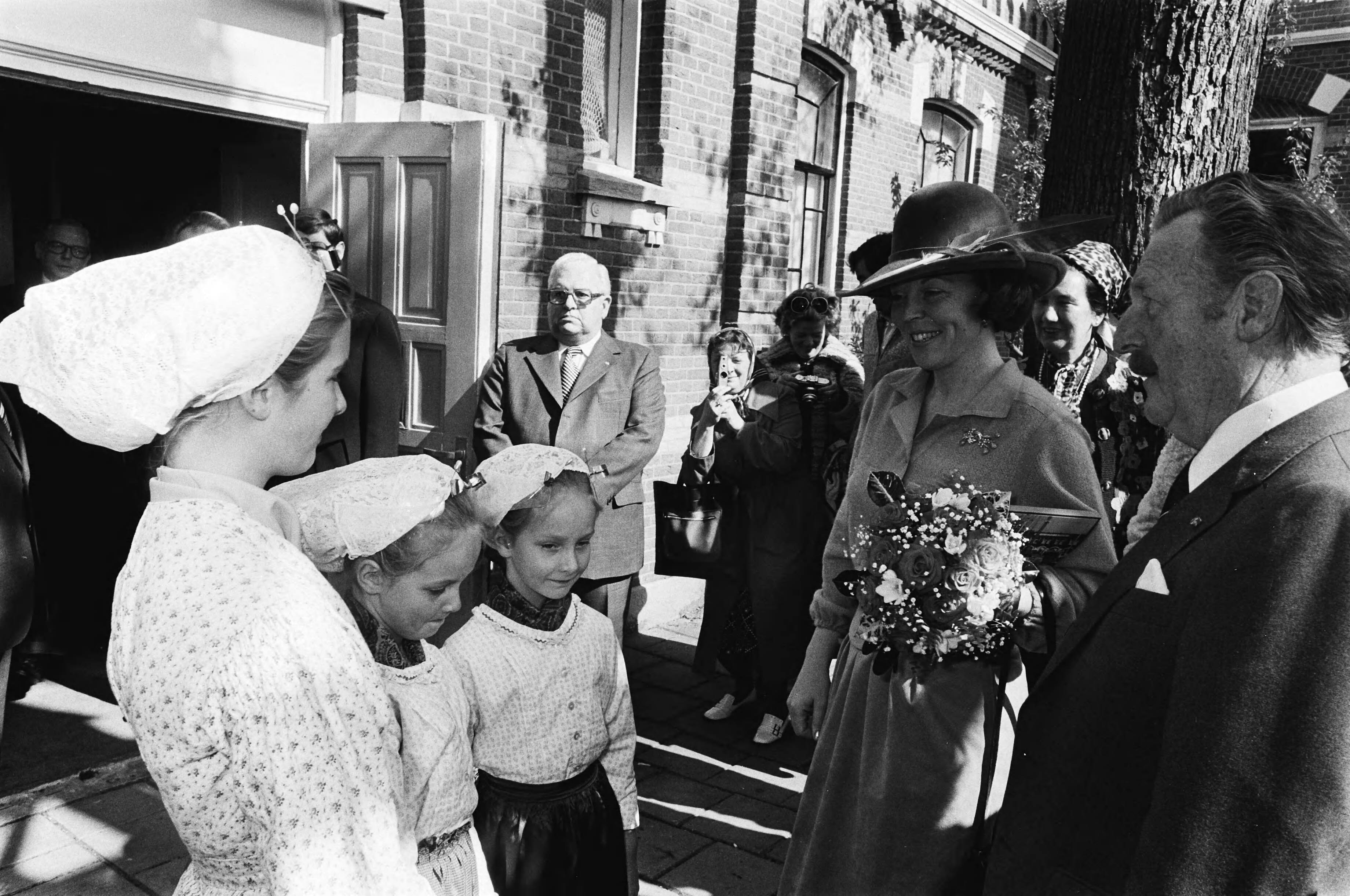 Prinses Beatrix onthult het monument "75 jaar havens" in Scheveningen — Prinses Beatrix krijgt een boek van kinderen in klederdracht — Foto: Suyk, Koen / Anefo. Licentie: Set B: Rechtenvrij / Publiek Domein. Bron: Nationaal Archief. http://hdl.handle.net/10648/acc9c52a-d0b4-102d-bcf8-003048976d84