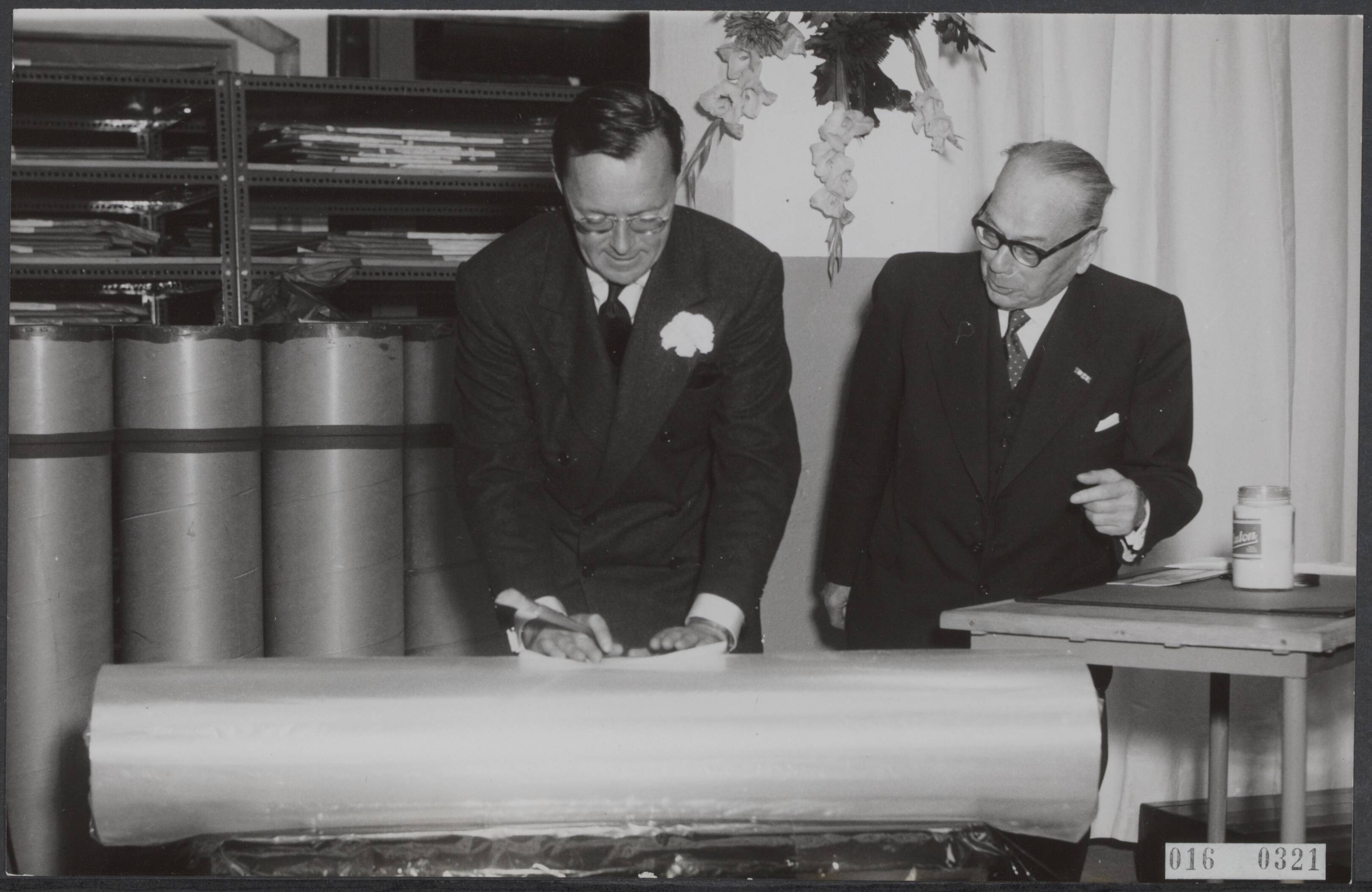 Fotocollectie Elsevier Binnenland — Prins Bernhard stelde in Breda de nieuwe Cellophaanfabriek van de Hollandse-Kunstzijde-Indusrie in bedrijf. Als opening bevestigde de prins een etiket op den bobine-cellophaan. Naast de prins directeur mr. R. van Maanen — Foto: Pot, Harry / Anefo. Licentie: Set B: Rechtenvrij / Publiek Domein. Bron: Nationaal Archief. http://hdl.handle.net/10648/adb9072a-d0b4-102d-bcf8-003048976d84
