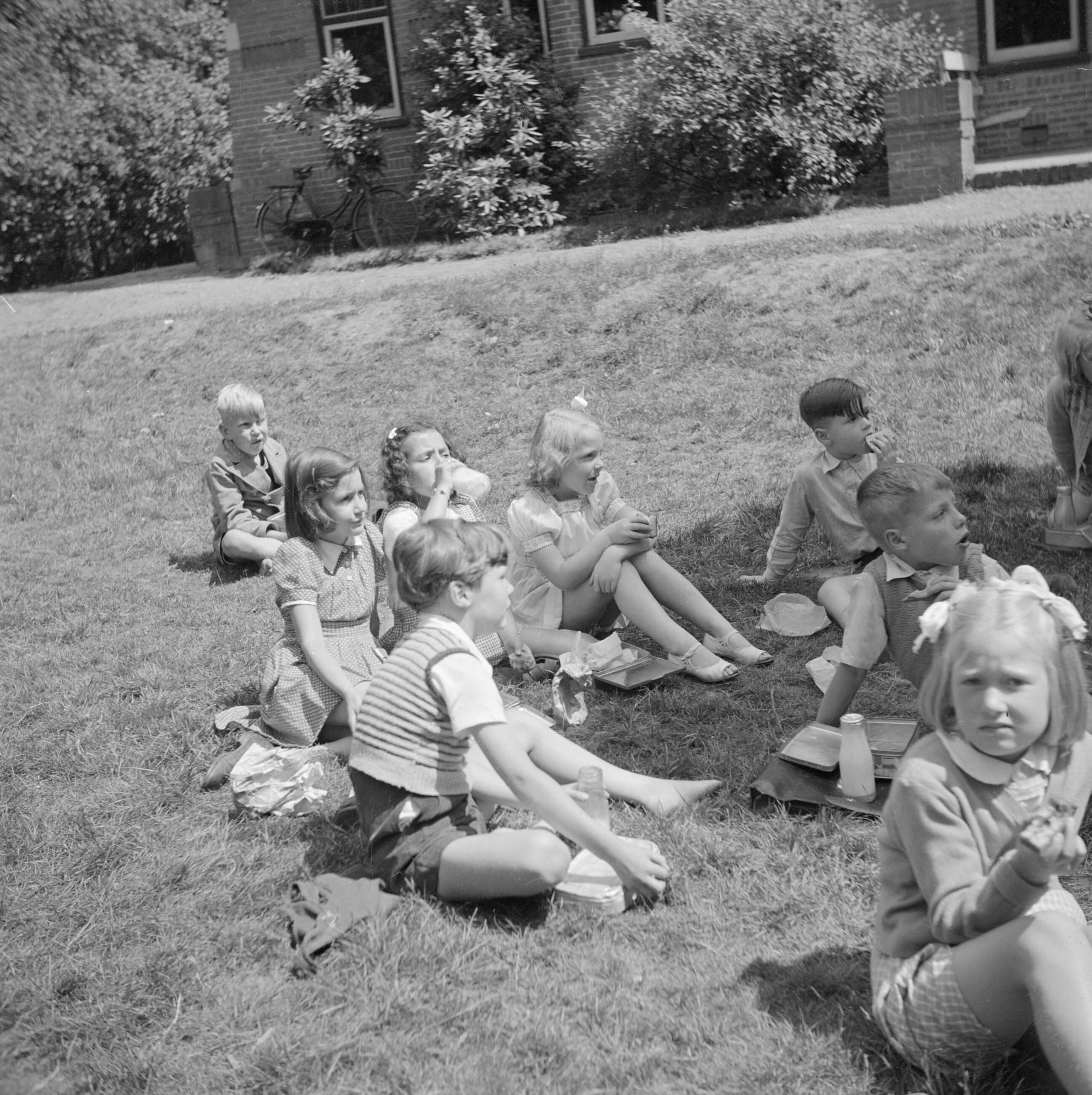 De prinsessen Beatrix en Irene op de Werkplaats Kindergemeenschap van Kees Boeke te Bilthoven — Prinses Irene en medeleerlingen pauzeren in de tuin — Foto: Poll, Willem van de. Licentie: Set B: Rechtenvrij / Publiek Domein. Bron: Nationaal Archief. http://hdl.handle.net/10648/aee80542-d0b4-102d-bcf8-003048976d84