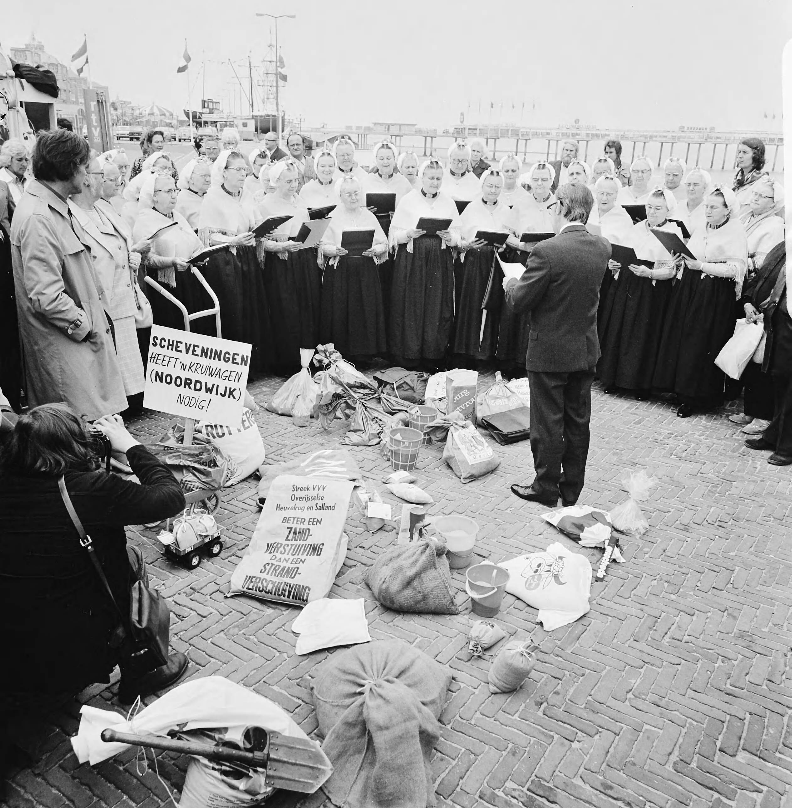 Fotocollectie Anefo — VVV-directeuren brengen zak zand naar jubilerende VVV in Scheveningen; tobben zand op boulevard en Schevenings zangkoor — Foto: Mieremet, Rob / Anefo. Licentie: Set B: Rechtenvrij / Publiek Domein. Bron: Nationaal Archief. http://hdl.handle.net/10648/ac4add46-d0b4-102d-bcf8-003048976d84