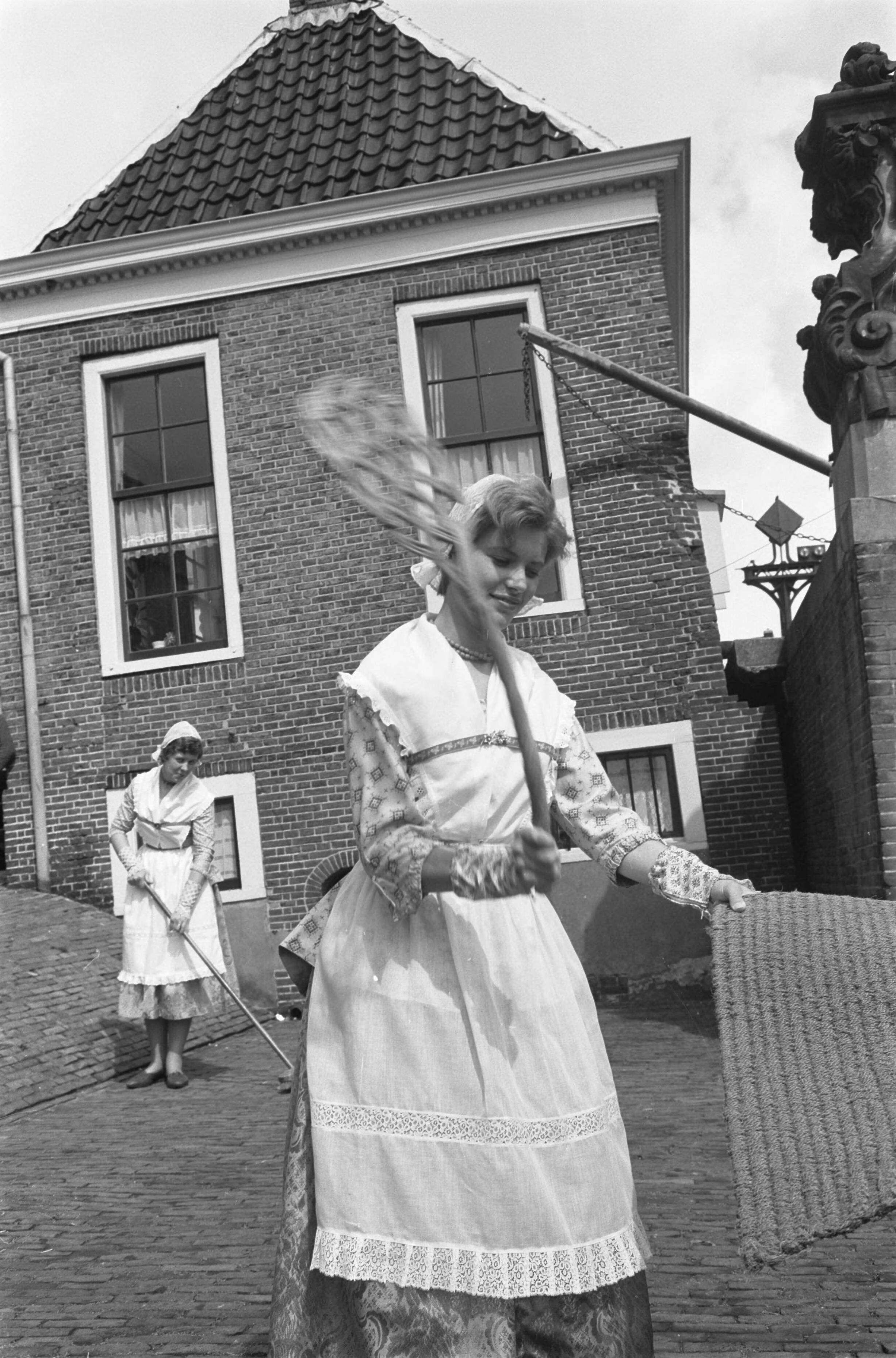 Fotocollectie Anefo — Voorbereidingen voor de feestelijkheden ter gelegenheid van viering 150 jaar stadsrechten van Zaandam. Een meisje in Noord-Hollandse klederdracht aan het mattenkloppen — Foto: Pot, Harry / Anefo. Licentie: Set B: Rechtenvrij / Publiek Domein. Bron: Nationaal Archief. http://hdl.handle.net/10648/a9d6a478-d0b4-102d-bcf8-003048976d84