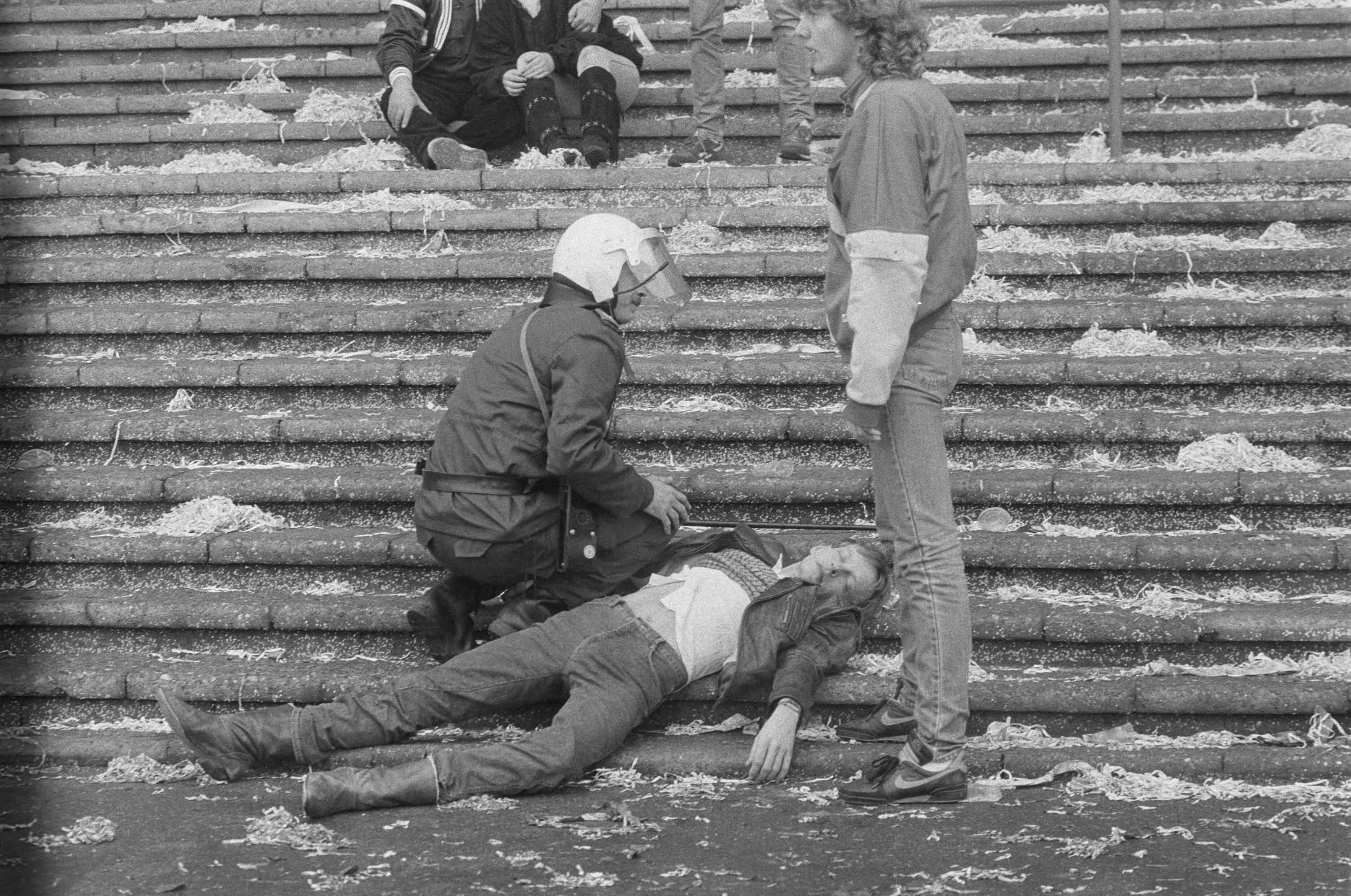 Fotocollectie Anefo — Supportersrellen tijdens Den Haag tegen Ajax in Den Haag ; een gewonde supporter ligt op de tribune na de rellen — Foto: Molendijk, Bart / Anefo. Licentie: Set B: Rechtenvrij / Publiek Domein. Bron: Nationaal Archief. http://hdl.handle.net/10648/ad5d5e34-d0b4-102d-bcf8-003048976d84