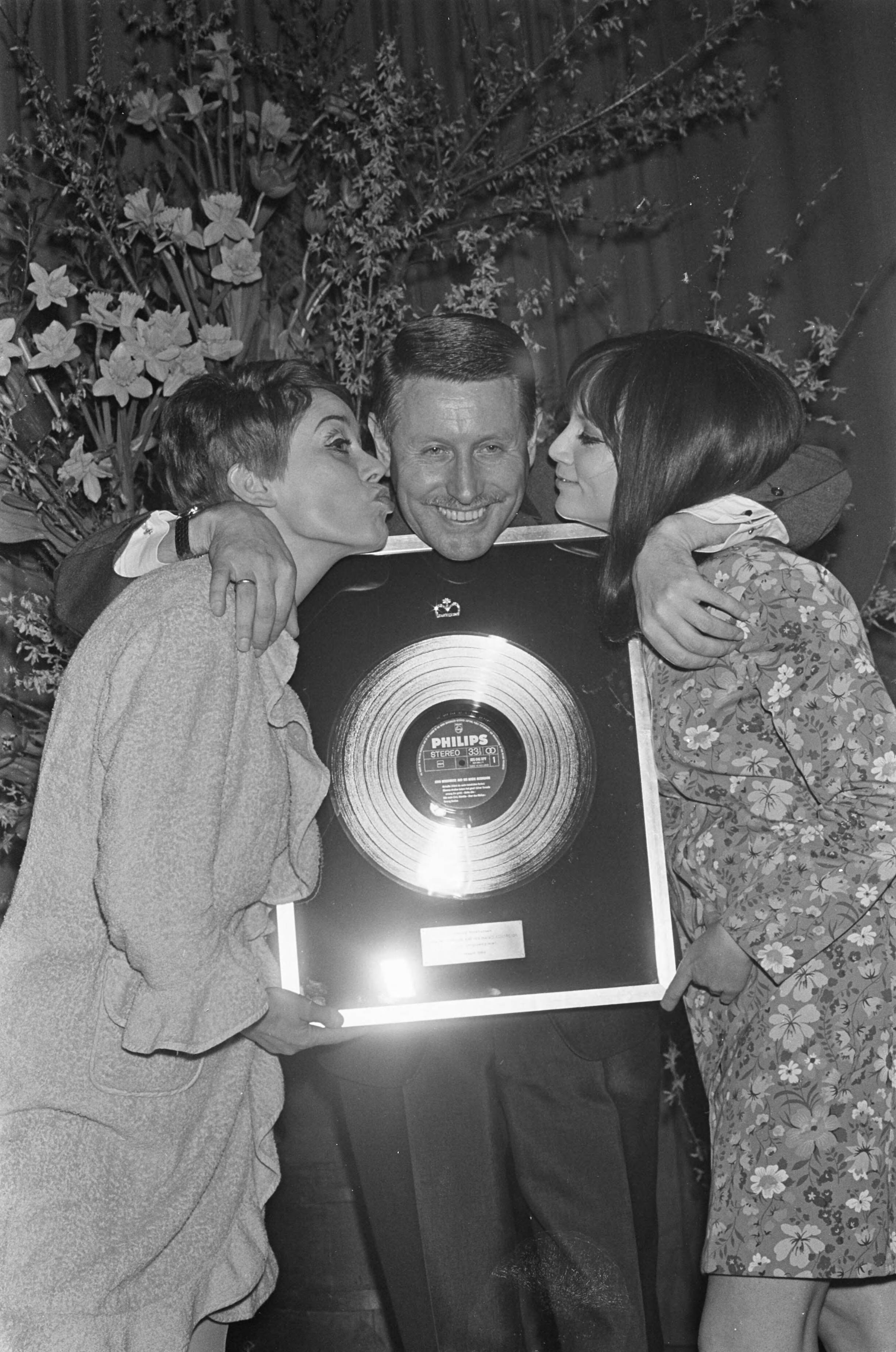 Fotocollectie Anefo — Platina plaat voor accordeonist John Woodhouse (Johan Hendrik Holshuysen) ; John gefeliciteerd door links Connie Vandenbos (Jacoba Adriana Hollestelle) en Thérèse Steinmetz te Laren — Foto: Kroon, Ron / Anefo. Licentie: Set B: Rechtenvrij / Publiek Domein. Bron: Nationaal Archief. http://hdl.handle.net/10648/ab39ed70-d0b4-102d-bcf8-003048976d84
