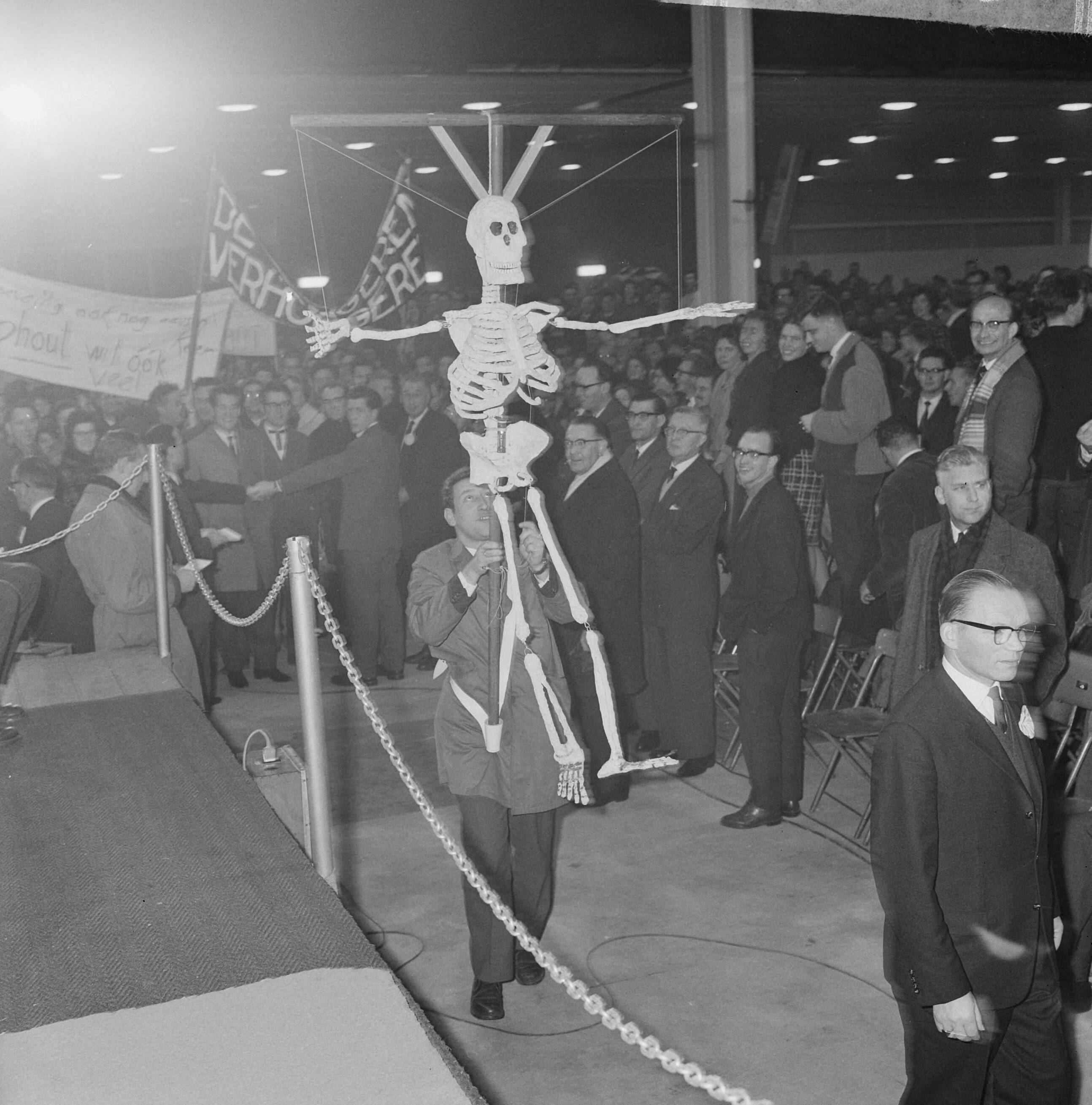 Fotocollectie Anefo — Onderwijzers demonstreren voor hogere salarissen in de Julianahal te Utrecht. Man met skelet — Foto: Koch, Eric / Anefo. Licentie: Set B: Rechtenvrij / Publiek Domein. Bron: Nationaal Archief. http://hdl.handle.net/10648/aa54f30a-d0b4-102d-bcf8-003048976d84
