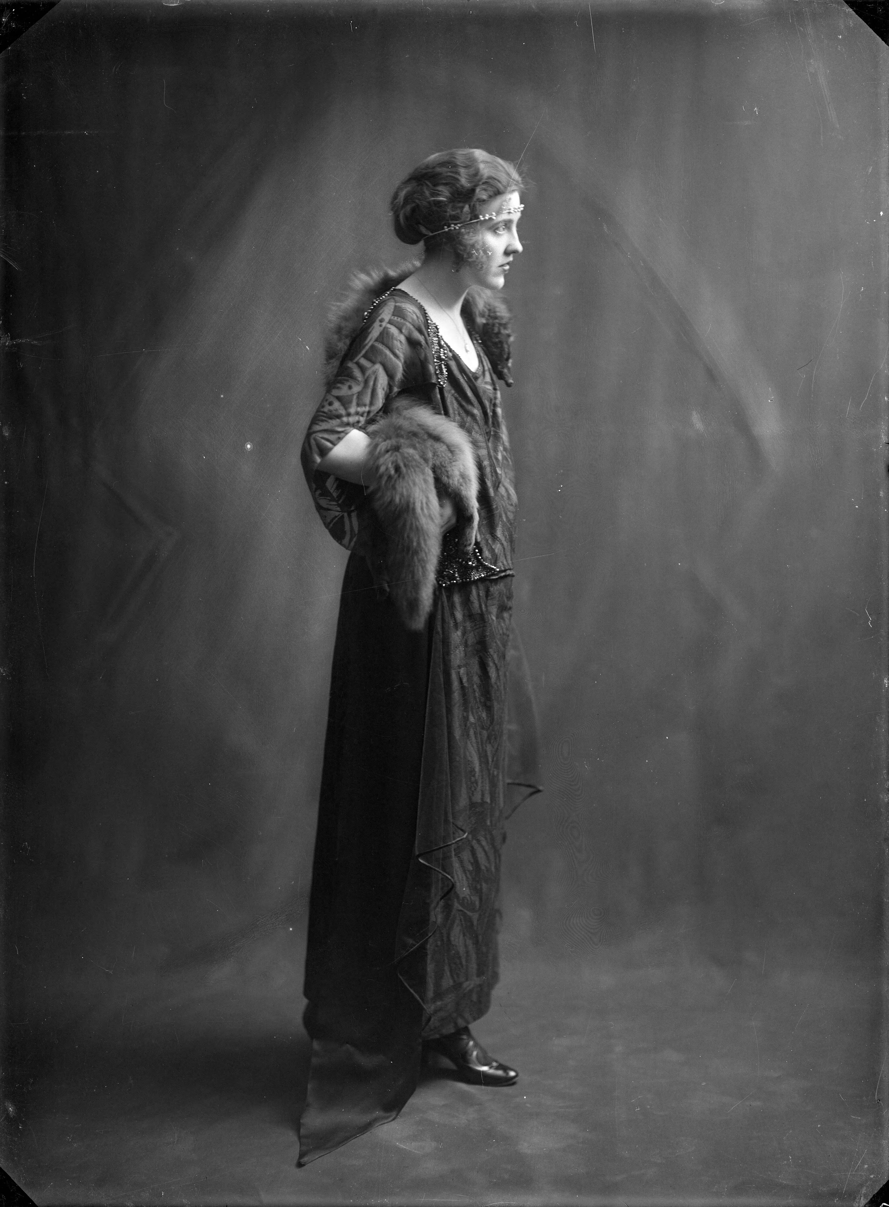 Berg, van den (BERG 050) — Studio-opnames. Dame in een lange jurk met ingeweven fluwelen art-decomotief op een transparante stof met gedrapeerd los voorpand. Om haar schouders een vos-bontstola. [Haarlem, Nederland, 1918-1930] — Foto: Berg, Th.C.J. van den / Spaarnestad Photo (05887). Licentie: Set B: Rechtenvrij / Publiek Domein. Bron: Nationaal Archief. http://hdl.handle.net/10648/35429da7-c547-a382-e063-6df0900a6686