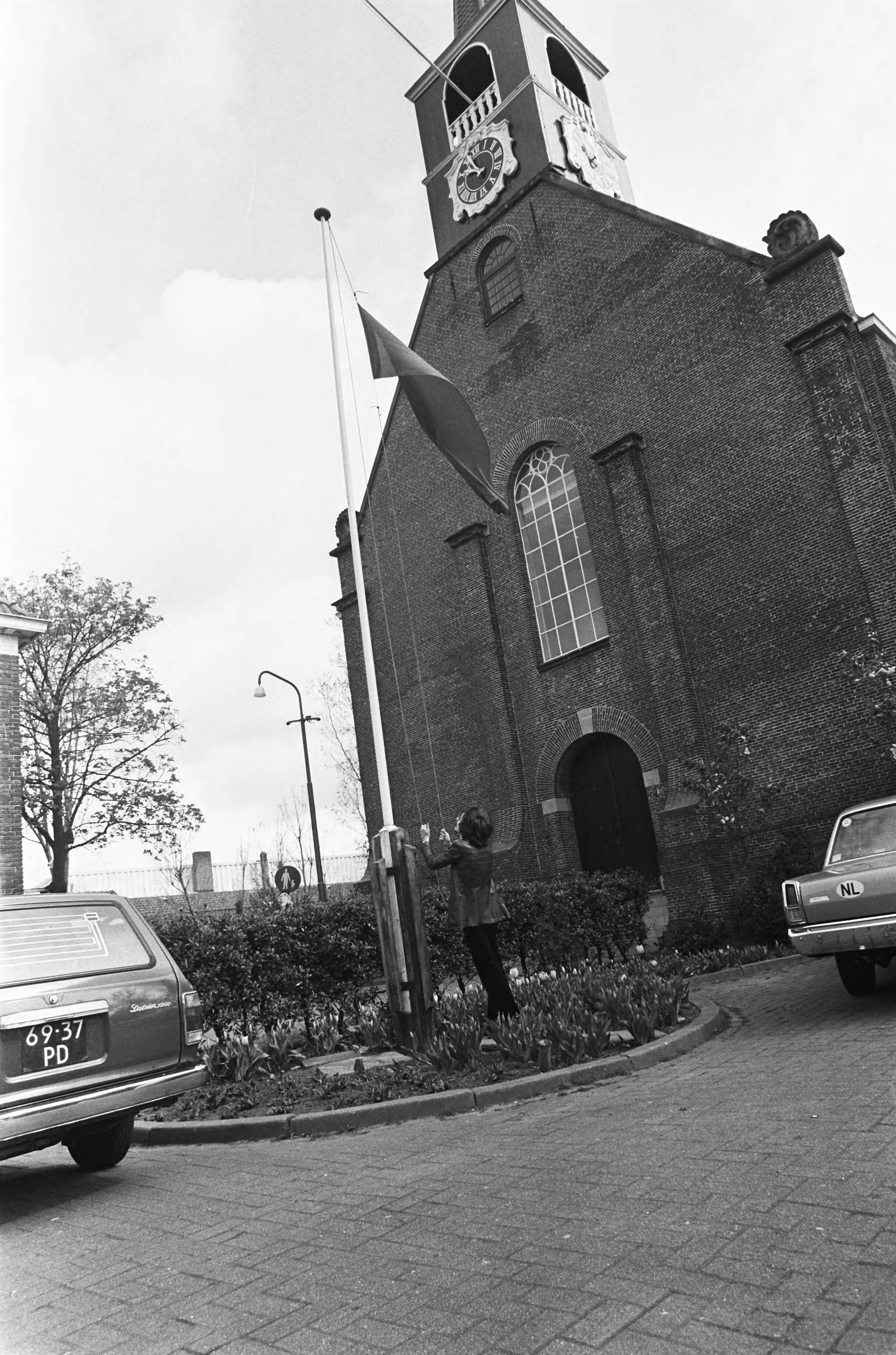 1 mei (Dag van de Arbeid) in Oostzaan — Hijsen van de rode vlag op het dorpsplein — Foto: Mieremet, Rob / Anefo. Licentie: Set B: Rechtenvrij / Publiek Domein. Bron: Nationaal Archief. http://hdl.handle.net/10648/ac67bb96-d0b4-102d-bcf8-003048976d84