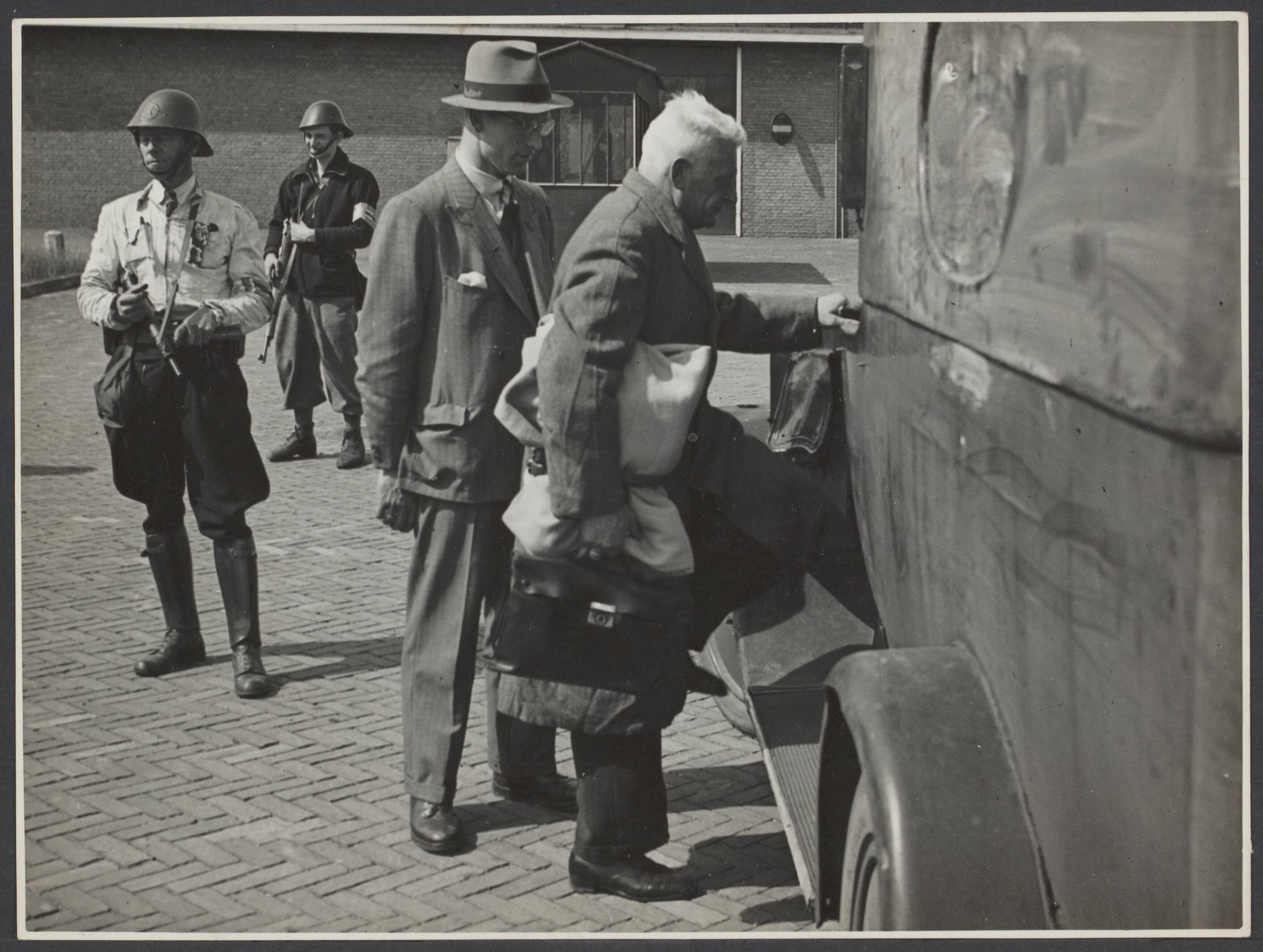 Collaboratie Nederland. — Haarlem [Een man (collaborateur) met aktetas stapt in een vrachtwagen. Achter hem een jongere man in burger. Zij worden bewaakt door leden van de Binnenlandse Strijdkrachten] — Foto: Nationaal Foto Persbureau (Stevens & Magielsen) / Rechtenvrij. Licentie: Set B: Rechtenvrij / Publiek Domein. Bron: Nationaal Archief. http://hdl.handle.net/10648/44f007fb-6401-4761-aa14-85cf6e90b830