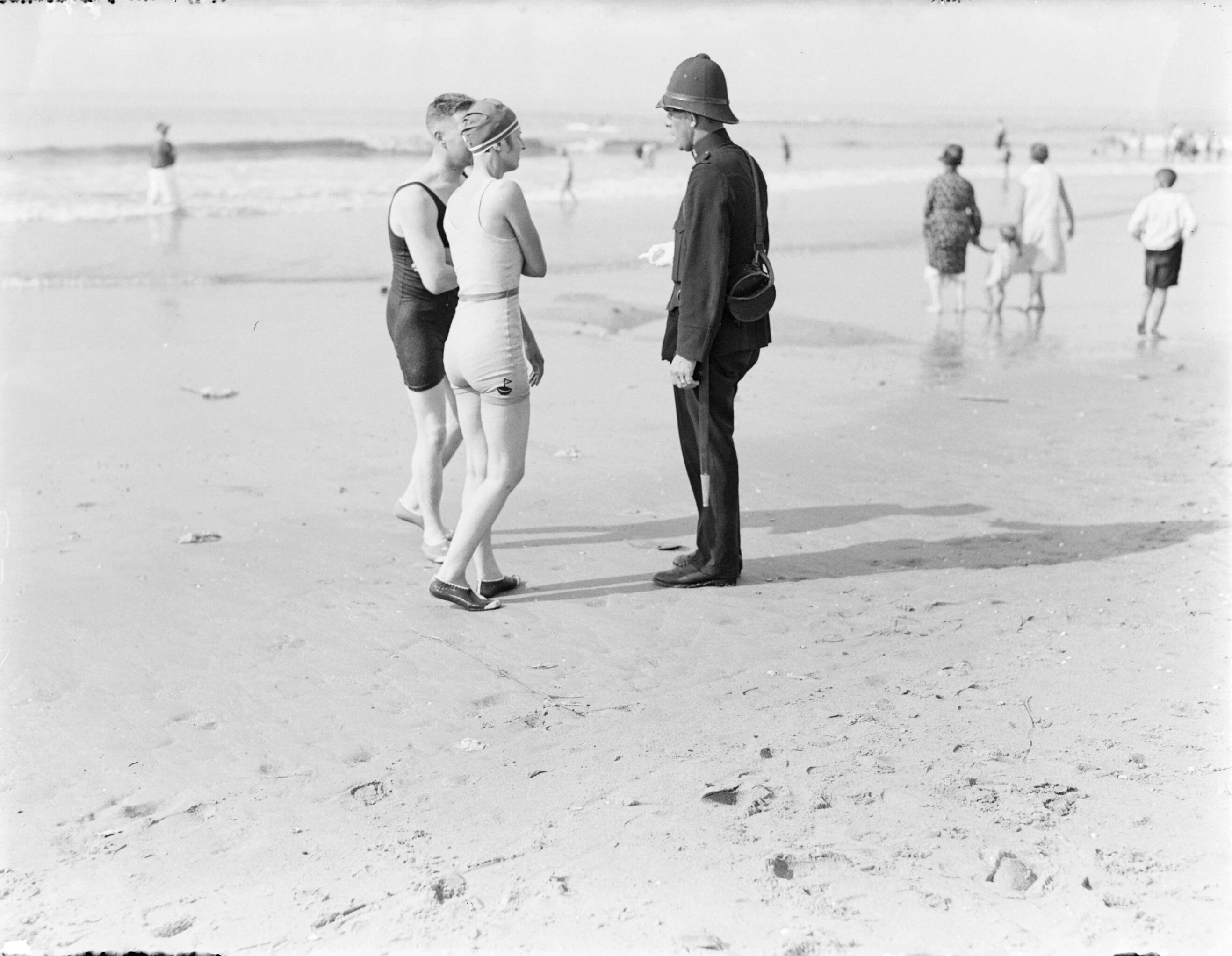 Strandtaferelen Scheveningen — Twee badgasten spreken met agent Jaspers (met reddingslijn op zijn rug) — Foto: Poll, Willem van de. Licentie: Set B: Rechtenvrij / Publiek Domein. Bron: Nationaal Archief. http://hdl.handle.net/10648/aea8616c-d0b4-102d-bcf8-003048976d84