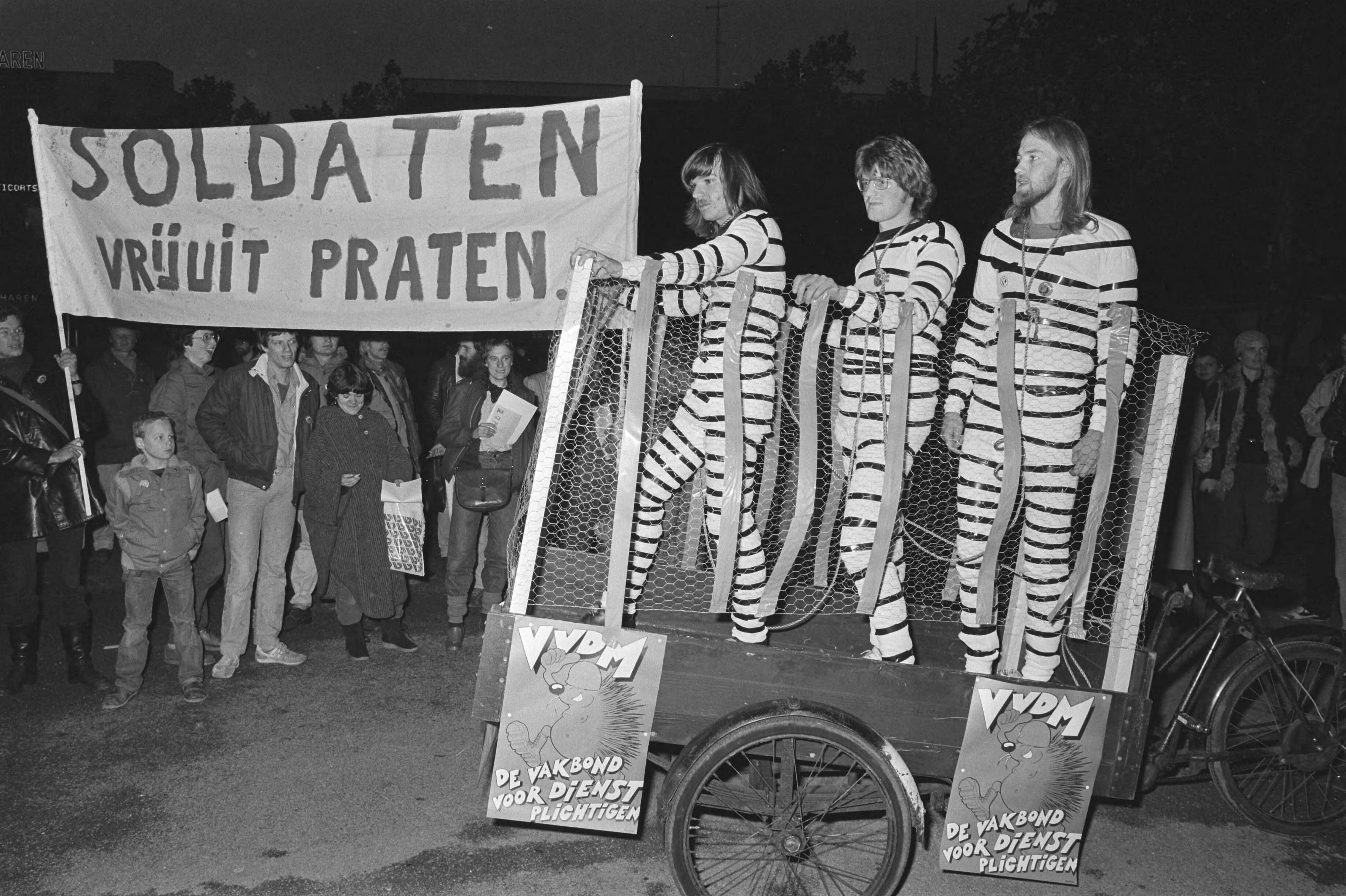 Demonstratie van de VVDM in Utrecht tegen de veroordeling door het Hoog Militair Gerechtshof van atoomweigeraar Aad Wijsman — Drie VVDM-ers, van links naar rechts Joost Cammeraat, Jan Bleumer en Jan van Beek, in gevangenispakken tijdens de demonstratie — Foto: Bogaerts, Rob / Anefo. Licentie: Set B: Rechtenvrij / Publiek Domein. Bron: Nationaal Archief. http://hdl.handle.net/10648/ad0719f2-d0b4-102d-bcf8-003048976d84