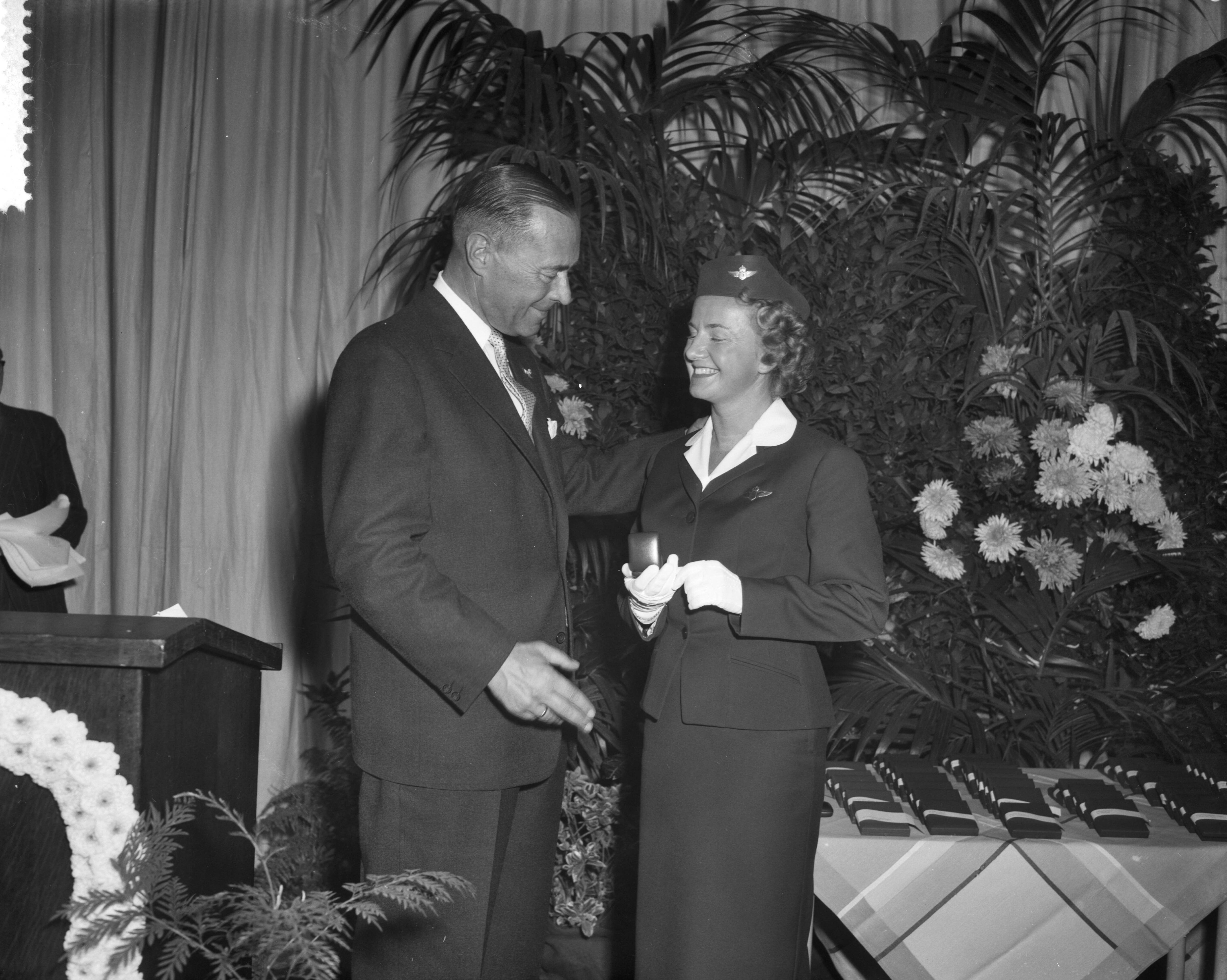 Fotocollectie Anefo — Uitreiking vliegurenpenningen KLM in de kantine van Schiphol. I.A. Aler, president-directeur van de KLM met chef-stewardess Marie Louise Crefcoeur, al 12 jaar in dienst. Zij ontvangt de gouden penning voor meer dan 10.000 vlieguren — Foto: Behrens, Herbert F. / Anefo. Licentie: Set B: Rechtenvrij / Publiek Domein. Bron: Nationaal Archief. http://hdl.handle.net/10648/a99efe4c-d0b4-102d-bcf8-003048976d84