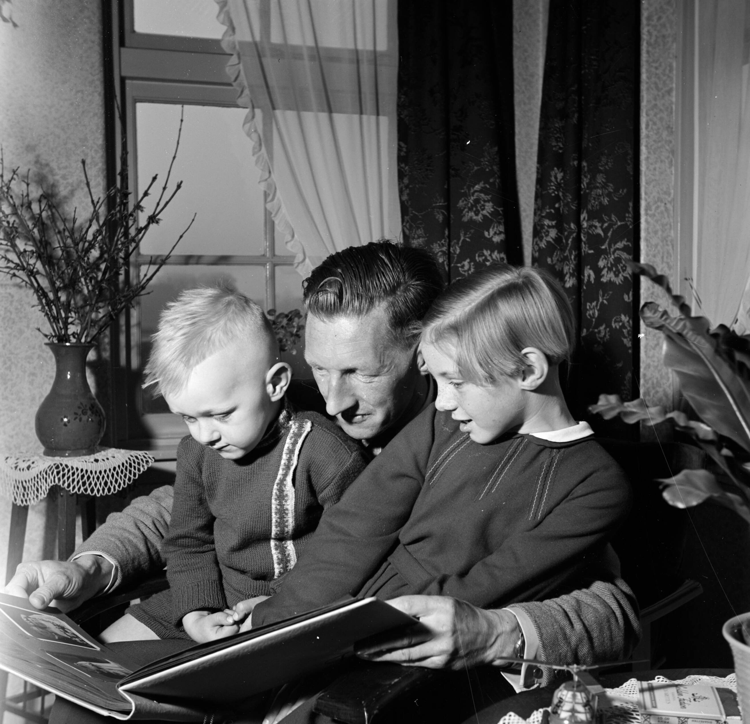 Fotocollectie Van de Poll — Gerard met zijn beide kinderen Gerrie en Marietje op schoot terwijl ze een fotoalbum bekijken — Foto: Poll, Willem van de. Licentie: Set B: Rechtenvrij / Publiek Domein. Bron: Nationaal Archief. http://hdl.handle.net/10648/aeccd222-d0b4-102d-bcf8-003048976d84