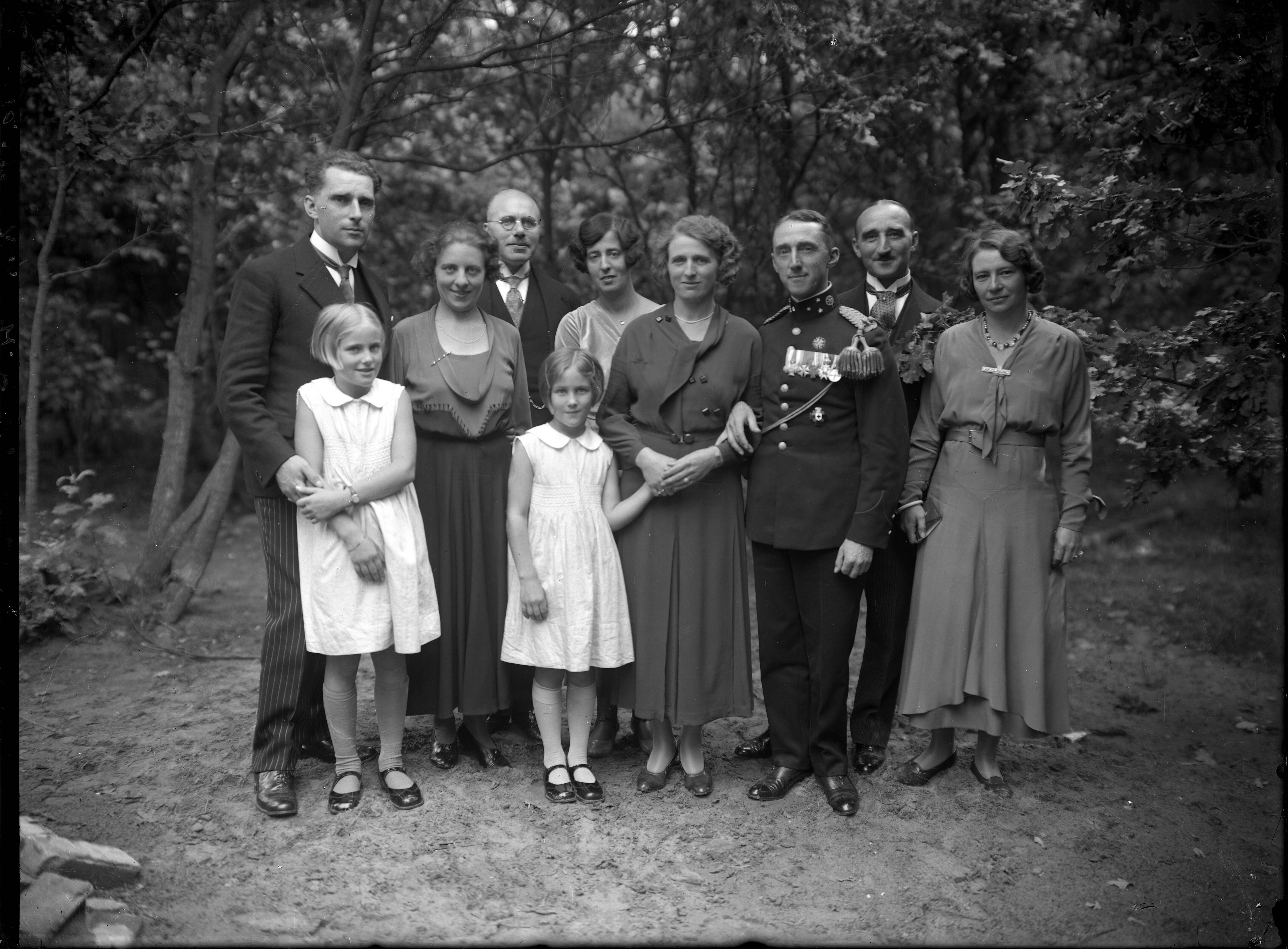 Portretten — Familieportretten. Buitenopname van een familie, man in uniform (rang kapitein) en de andere in pakken, vrouwen in enkellange jurken en twee jonge meisjes in witte mouwloze jurkjes.Nederland. 1918-1930. 10.033 Kap. H. Polis gravure — Foto: Berg, Th.C.J. van den / Spaarnestad Photo (05887). Licentie: Set B: Rechtenvrij / Publiek Domein. Bron: Nationaal Archief. http://hdl.handle.net/10648/35429da7-c769-a382-e063-6df0900a6686