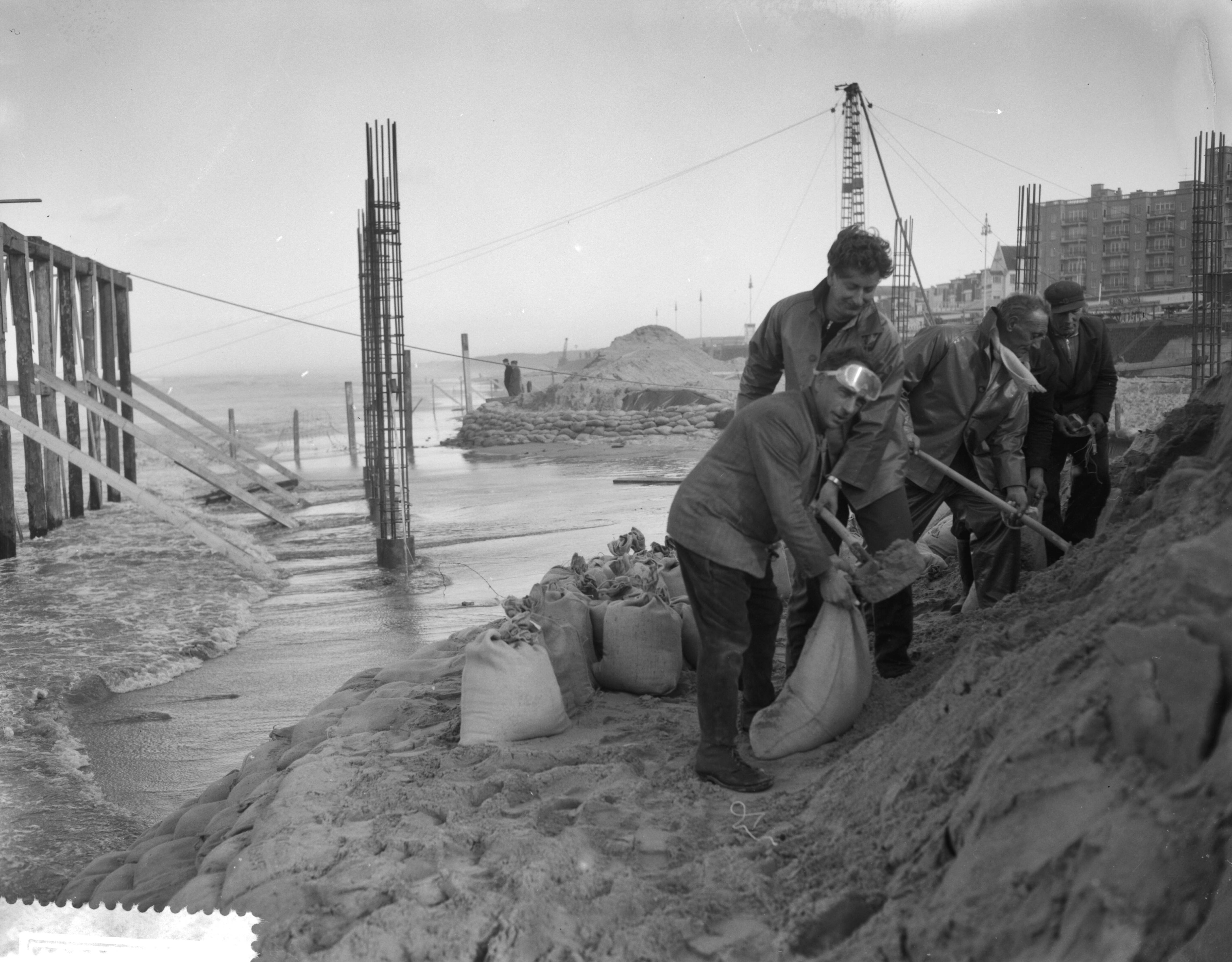 Fotocollectie Anefo — Bouw pier Scheveningen stagneert door storm. Dijkversterkingen met zandzakken — Foto: Bilsen, Joop van / Anefo. Licentie: Set B: Rechtenvrij / Publiek Domein. Bron: Nationaal Archief. http://hdl.handle.net/10648/a9a0c8bc-d0b4-102d-bcf8-003048976d84