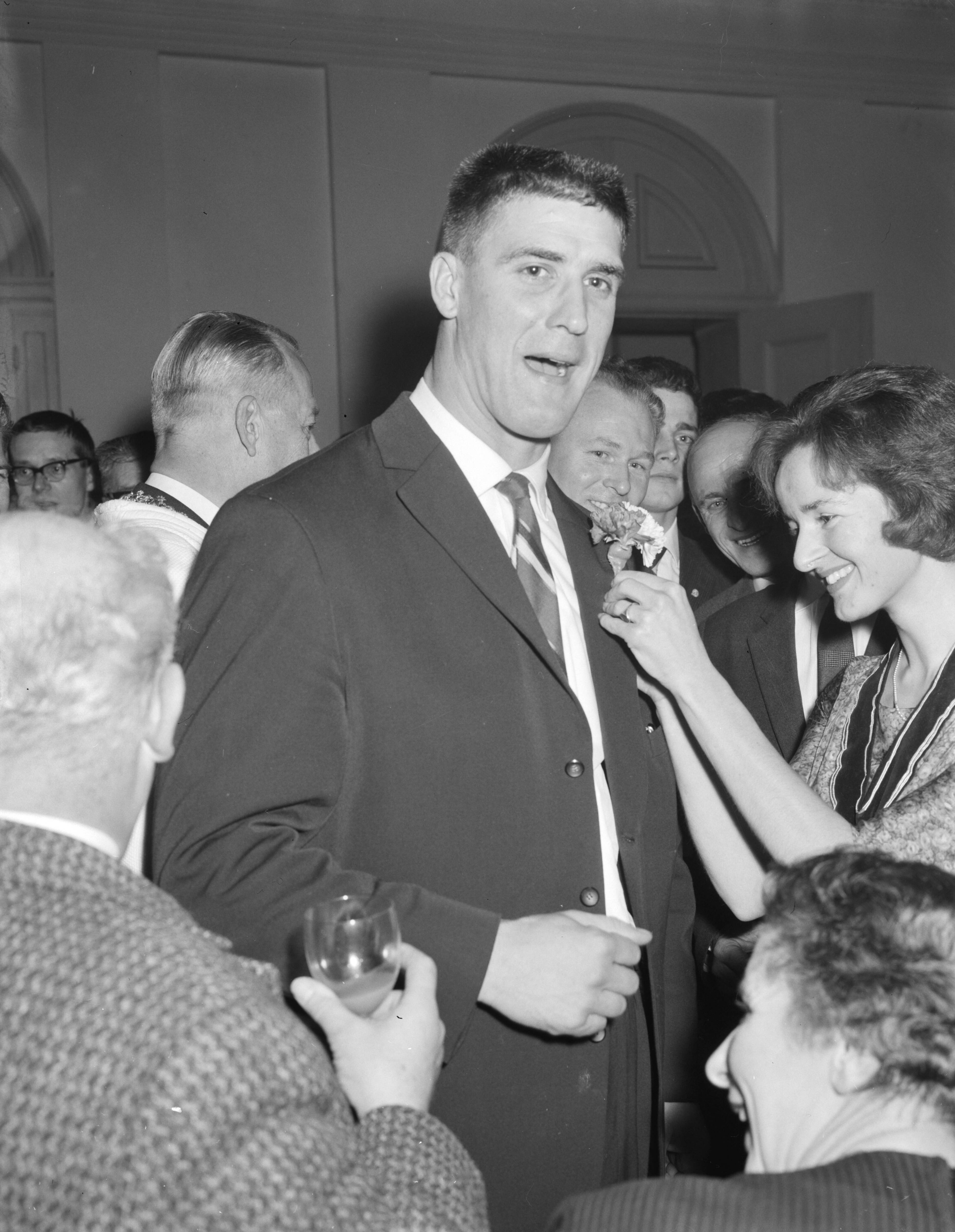 Fotocollectie Anefo — Huldiging van Anton Geesink op het stadhuis van Utrecht. Studente speldt een corsage op de rever van Anton Geesink — Foto: Rossem, Wim van / Anefo. Licentie: Set B: Rechtenvrij / Publiek Domein. Bron: Nationaal Archief. http://hdl.handle.net/10648/a9eed958-d0b4-102d-bcf8-003048976d84