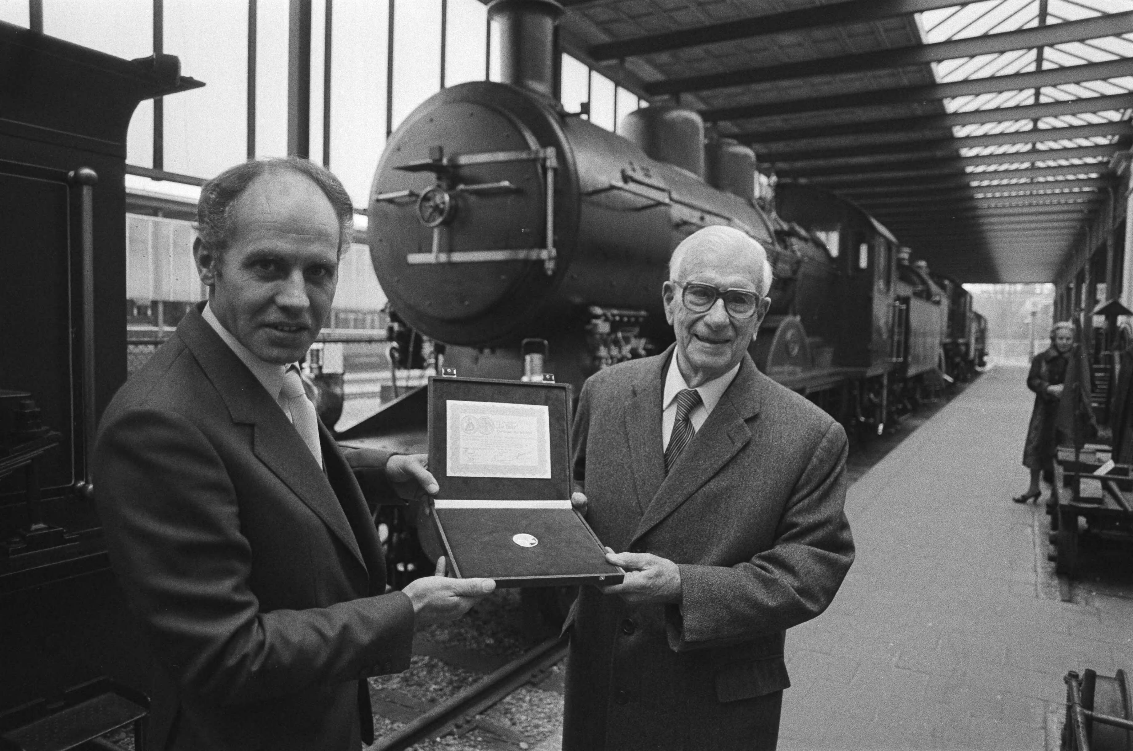 Fotocollectie Anefo — Dr.ir.F.Q. Den Hollander (oud-president NS) (r.) krijgt in het Spoorwegmuseum in Utrecht 1ste exemplaar serie US-herdenkingsmunten door E. M. Meupelerberg / — Foto: Antonisse, Marcel / Anefo. Licentie: Set B: Rechtenvrij / Publiek Domein. Bron: Nationaal Archief. http://hdl.handle.net/10648/ad10224a-d0b4-102d-bcf8-003048976d84