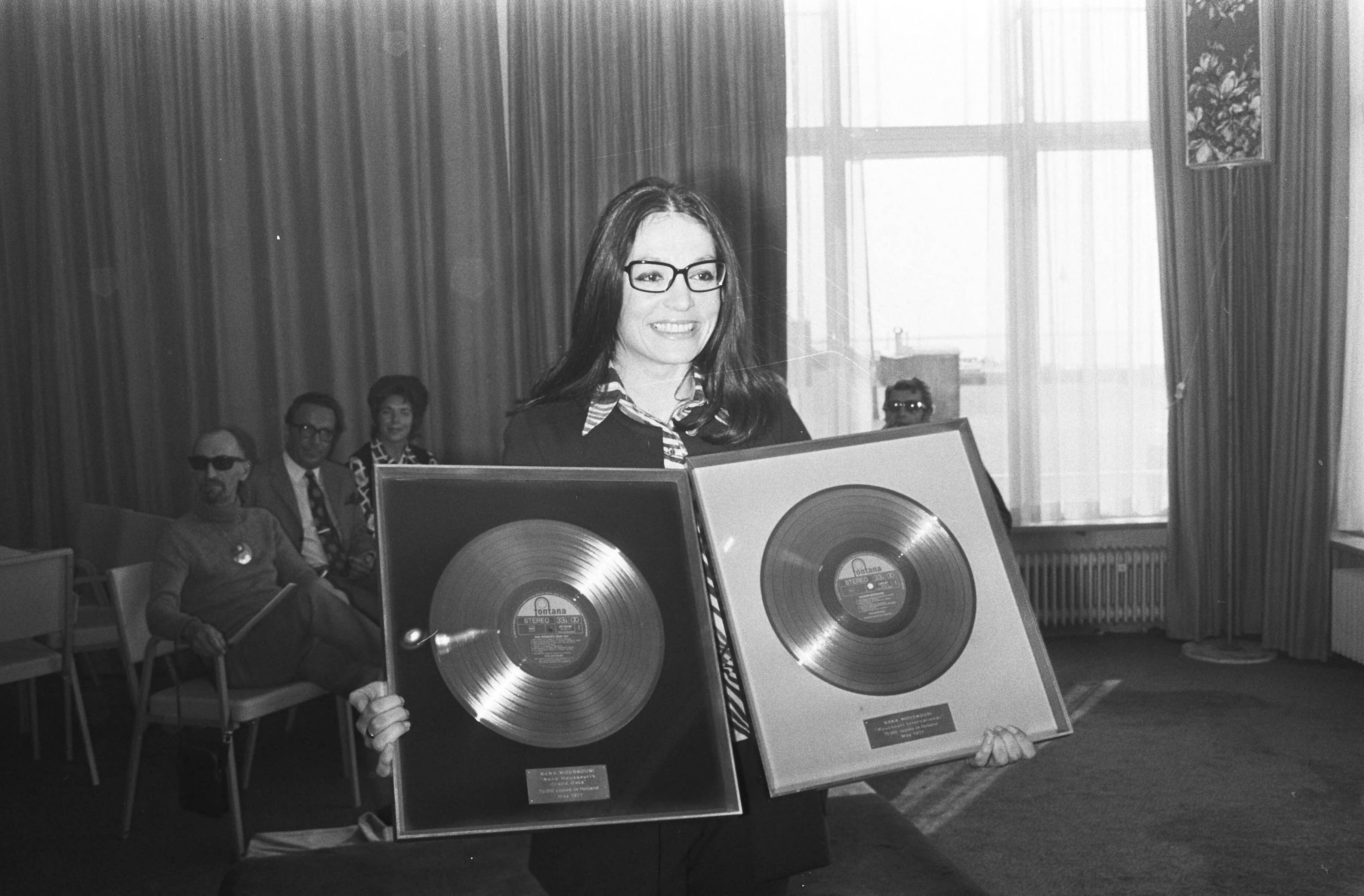 Nana Mouskouri krijgt een gouden en een platina plaat in het Kurhaus te — Nana Mouskouri toont haar platen — Foto: Fotograaf Onbekend / Anefo. Licentie: Set B: Rechtenvrij / Publiek Domein. Bron: Nationaal Archief. http://hdl.handle.net/10648/abbf498e-d0b4-102d-bcf8-003048976d84