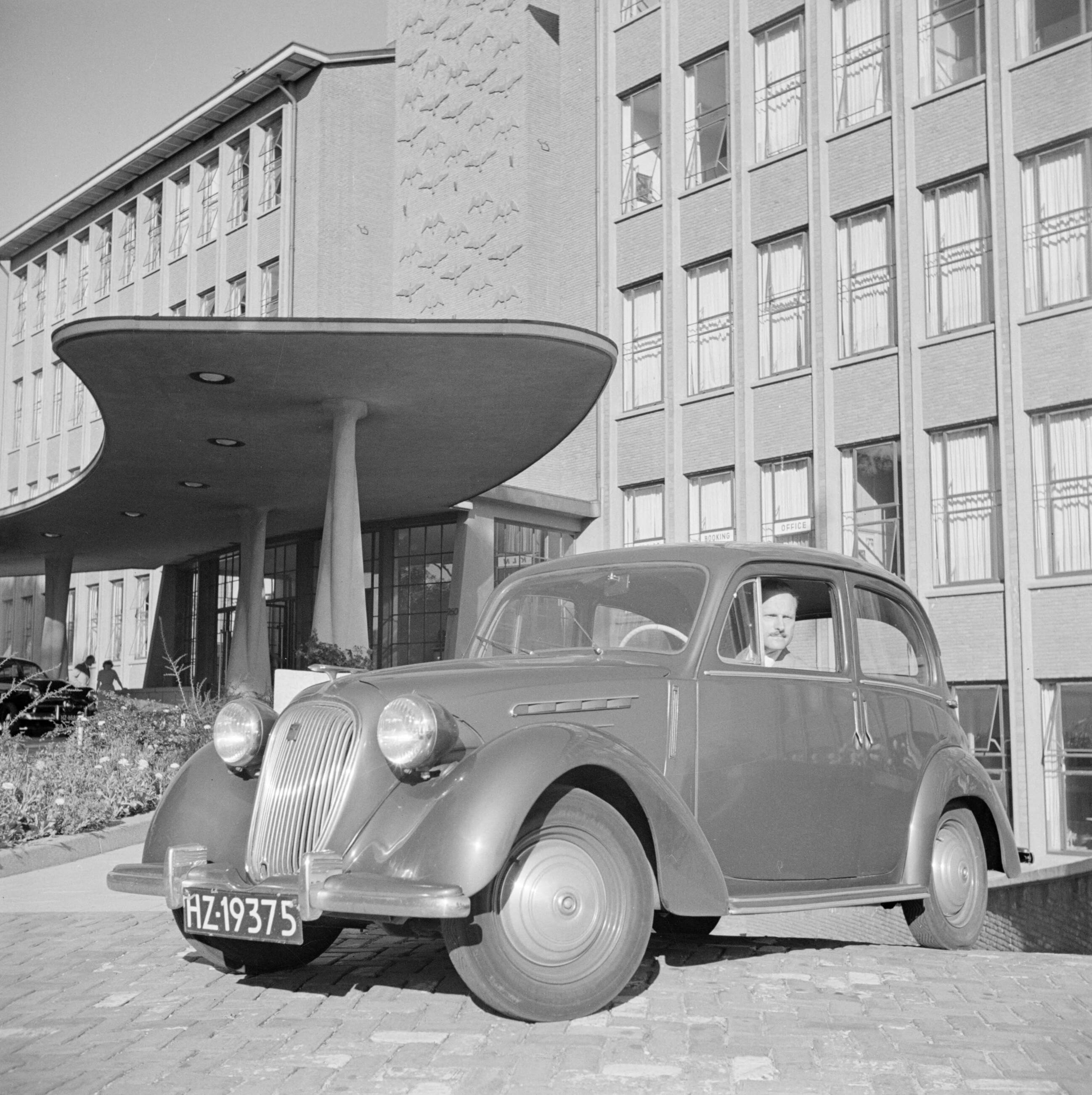 KLM personeel huisstijl en Schiphol — De heer de Visser in zijn Simca 8 voor het KLM hoofdgebouw in Den Haag — Foto: Poll, Willem van de. Licentie: Set B: Rechtenvrij / Publiek Domein. Bron: Nationaal Archief. http://hdl.handle.net/10648/aeeca0f2-d0b4-102d-bcf8-003048976d84
