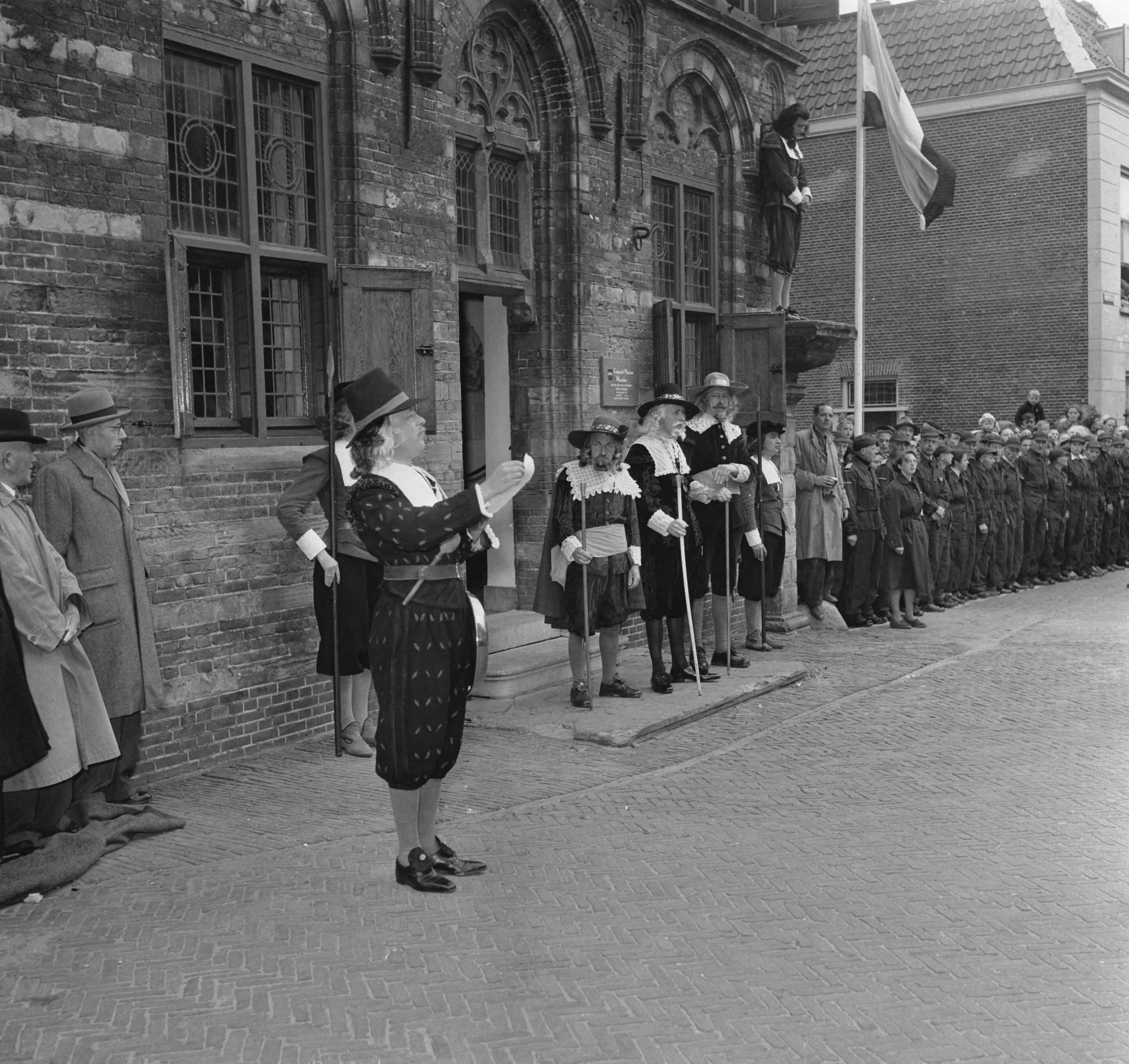 Koninklijk bezoek aan 15 gemeentes in Zuid-Holland (Rijnstreek en Merengebied) — Koningin Juliana en prins Bernhard bezoeken Woerden. Voor het oude gerechtsgebouw (gemeentemuseum) worden zij toegesproken door een heraut van "schout en schepenen" — Foto: Noske, J.D. / Anefo. Licentie: Set B: Rechtenvrij / Publiek Domein. Bron: Nationaal Archief. http://hdl.handle.net/10648/a92231b4-d0b4-102d-bcf8-003048976d84