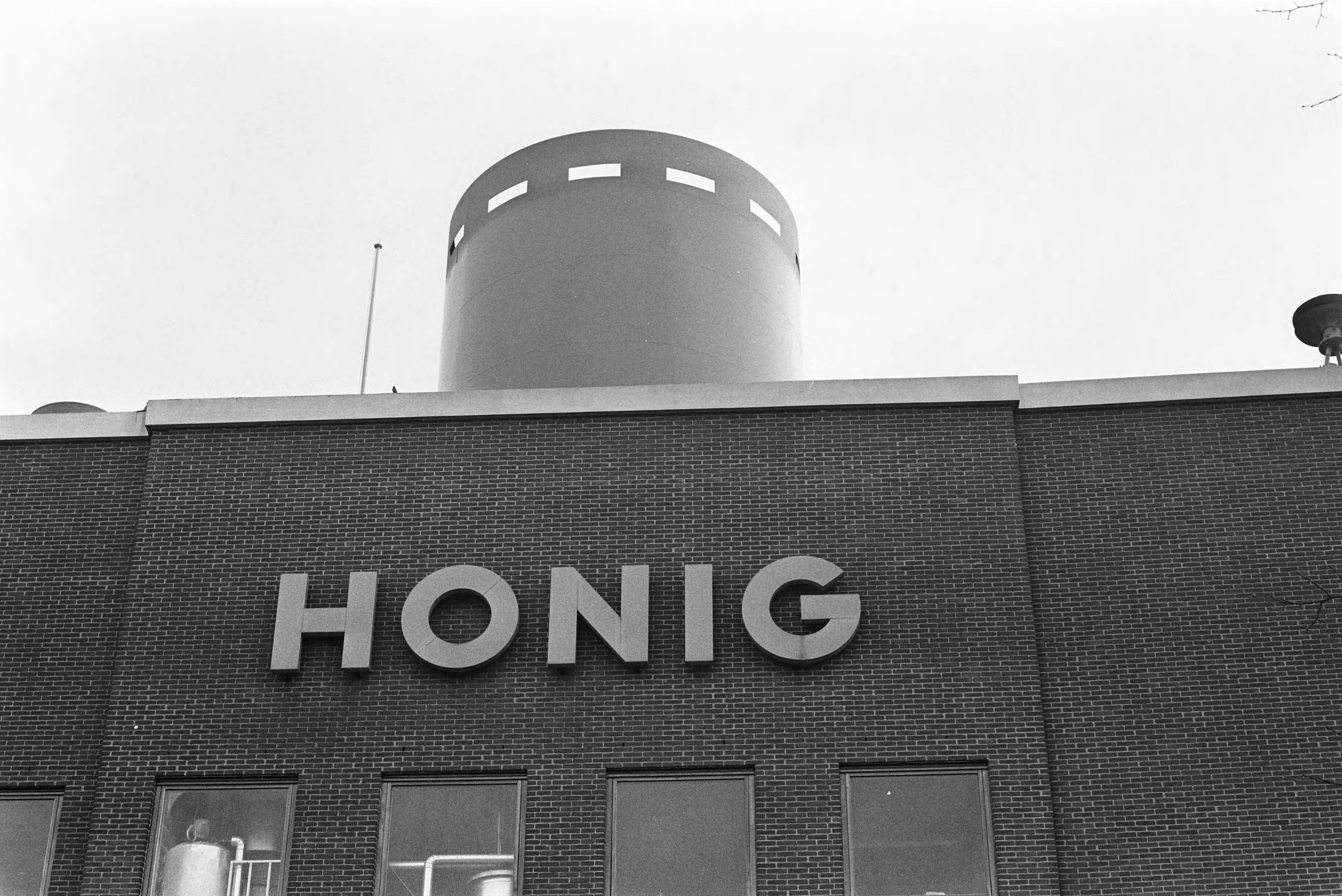Fotocollectie Anefo — Werknemers van Honig in Koog aan de Zaan staken voor 1% duurtetoeslag en werktijdverkorting aan eind van de dag. Exterieur opschrift "Honig" — Foto: Evers, Joost / Anefo. Licentie: Set B: Rechtenvrij / Publiek Domein. Bron: Nationaal Archief. http://hdl.handle.net/10648/ab8640a8-d0b4-102d-bcf8-003048976d84