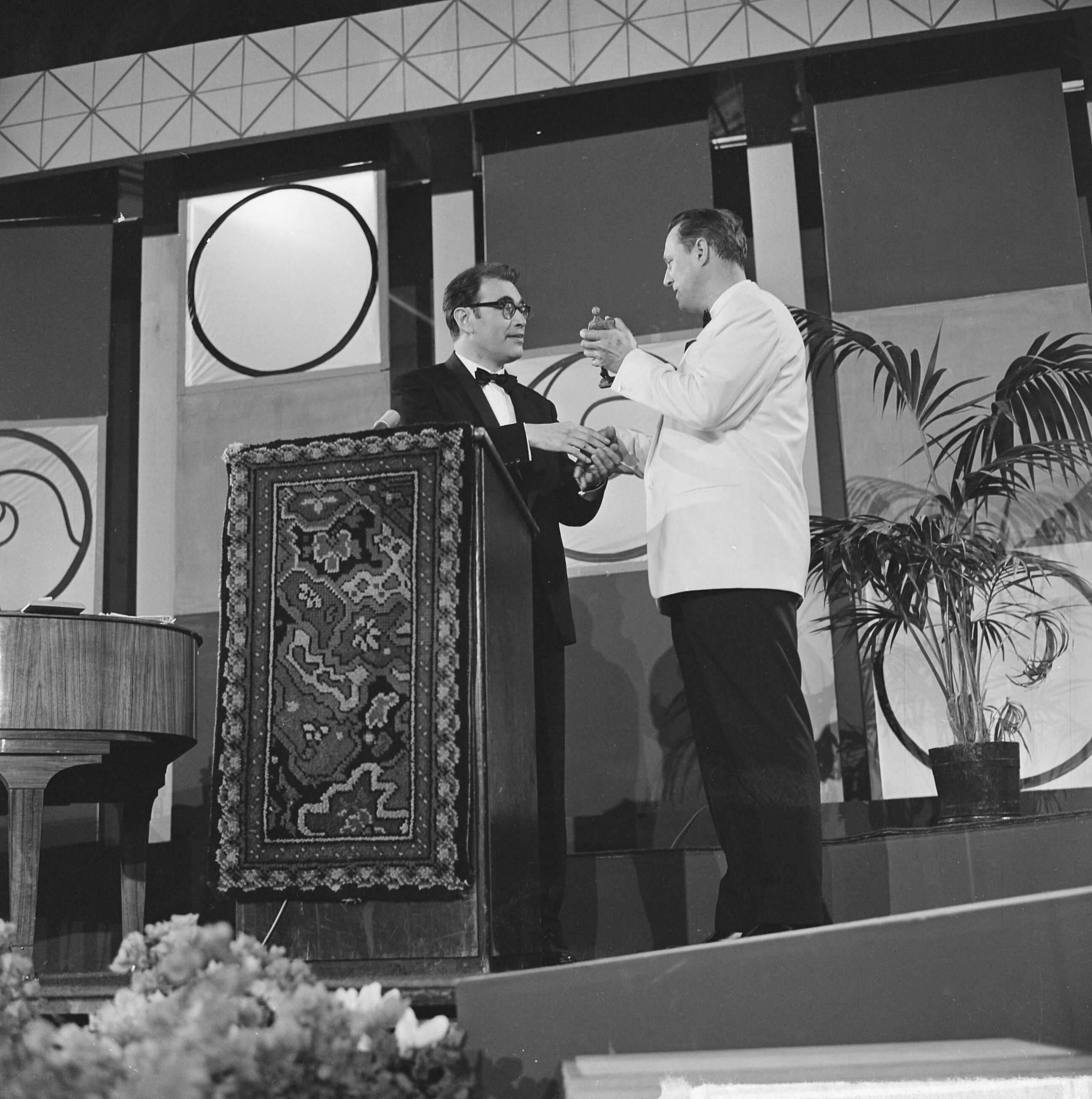 Grand Gala du Disque 1963 — Grand Gala du Disque Populair in het Kurhaus te Scheveningen. Peter Schilperoort (Dutch Swing College Band) biedt zijn Edison aan aan presentator Godfried Bomans — Foto: Koch, Eric / Anefo. Licentie: Set B: Rechtenvrij / Publiek Domein. Bron: Nationaal Archief. http://hdl.handle.net/10648/aa498448-d0b4-102d-bcf8-003048976d84