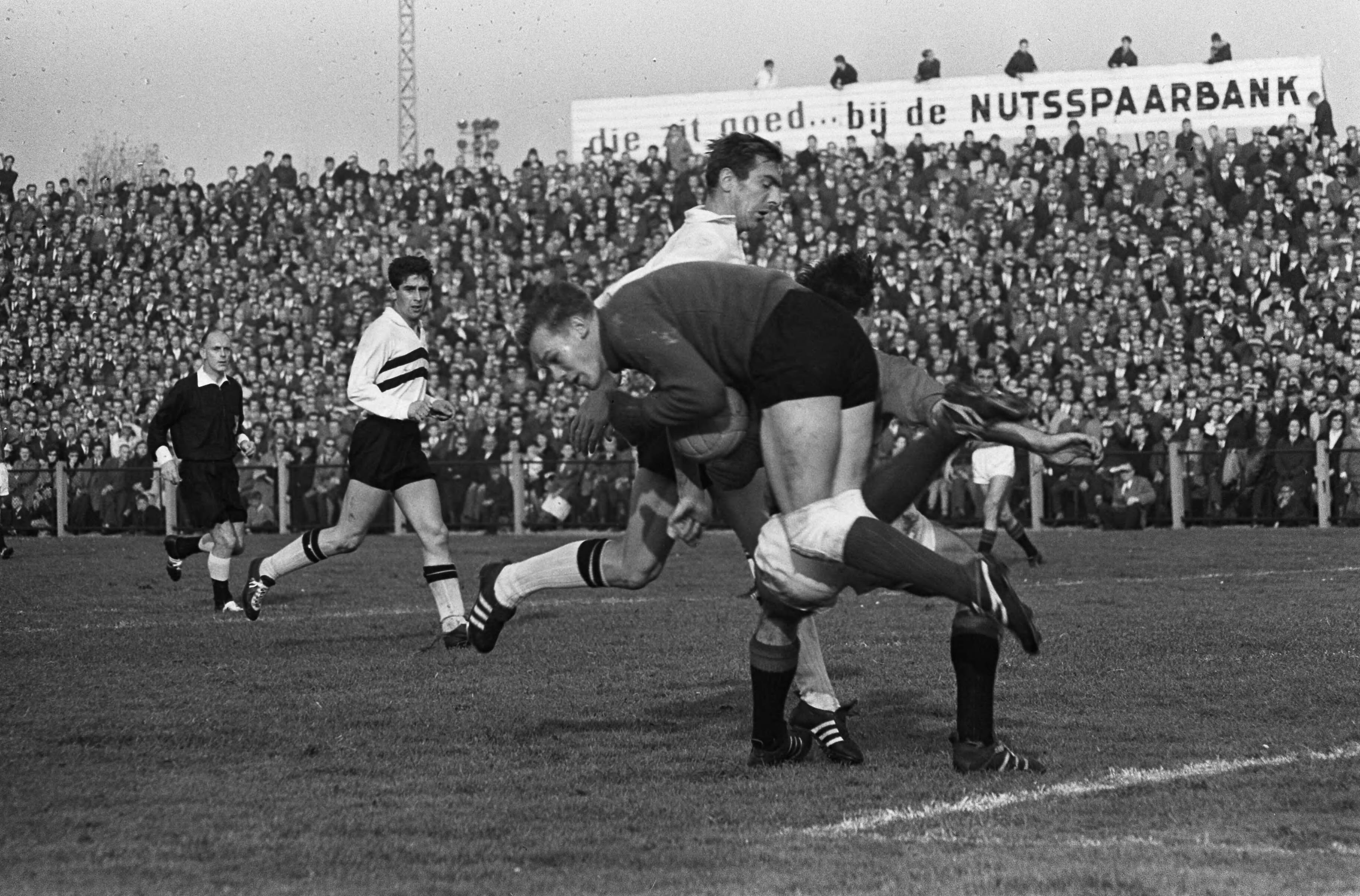 Fotocollectie Anefo — Voetbal. ADO tegen NAC 3-4. Keeper Peter van der Merwe (NAC) heeft bal klemvast. Peter Hoet (ADO) rechts achter hem en NAC-spil Dries Mul. Links Cock Luyten (NAC) — Foto: Koch, Eric / Anefo. Licentie: Set B: Rechtenvrij / Publiek Domein. Bron: Nationaal Archief. http://hdl.handle.net/10648/aa4c5268-d0b4-102d-bcf8-003048976d84