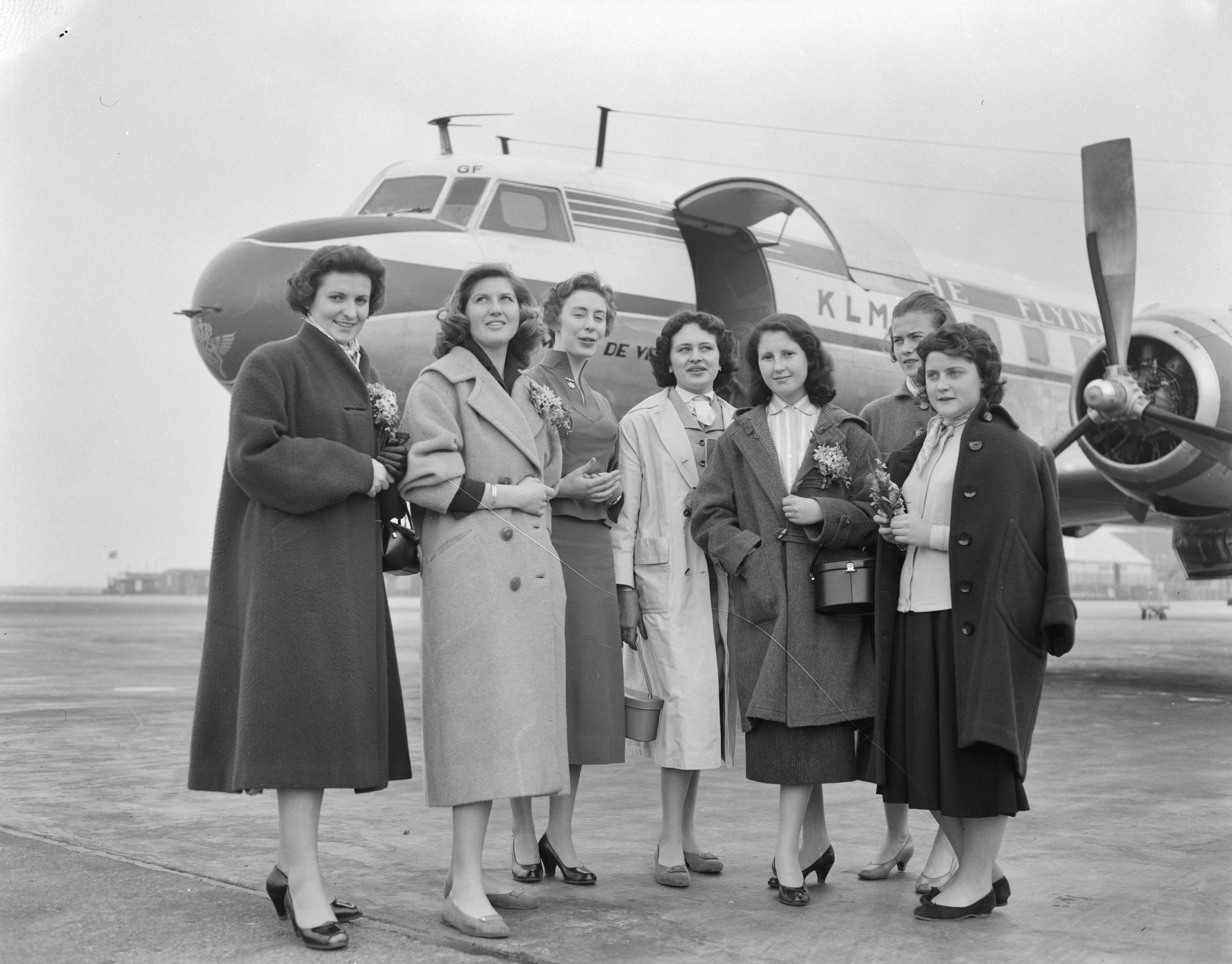 Fotocollectie Anefo — Zes jeugdige Franse meisjes, behorende tot de 20 Françaises, die winnaressen zijn geworden van de wereldcompetitie voor jonge meisjes, uitgeschreven door het Franse damesweekblad „Elle”, zijn met een toestel van de SAS op Schiphol aangekomen. Daar stond het Nederlandse „Doorsnee-meisje” winnares de 20-jarige Mia Kroon uit Hillegom, gereed met corsages samengesteld uit bollenbloemen — Foto: Rossem, Wim van / Anefo. Licentie: Set B: Rechtenvrij / Publiek Domein. Bron: Nationaal Archief. http://hdl.handle.net/10648/a9450702-d0b4-102d-bcf8-003048976d84