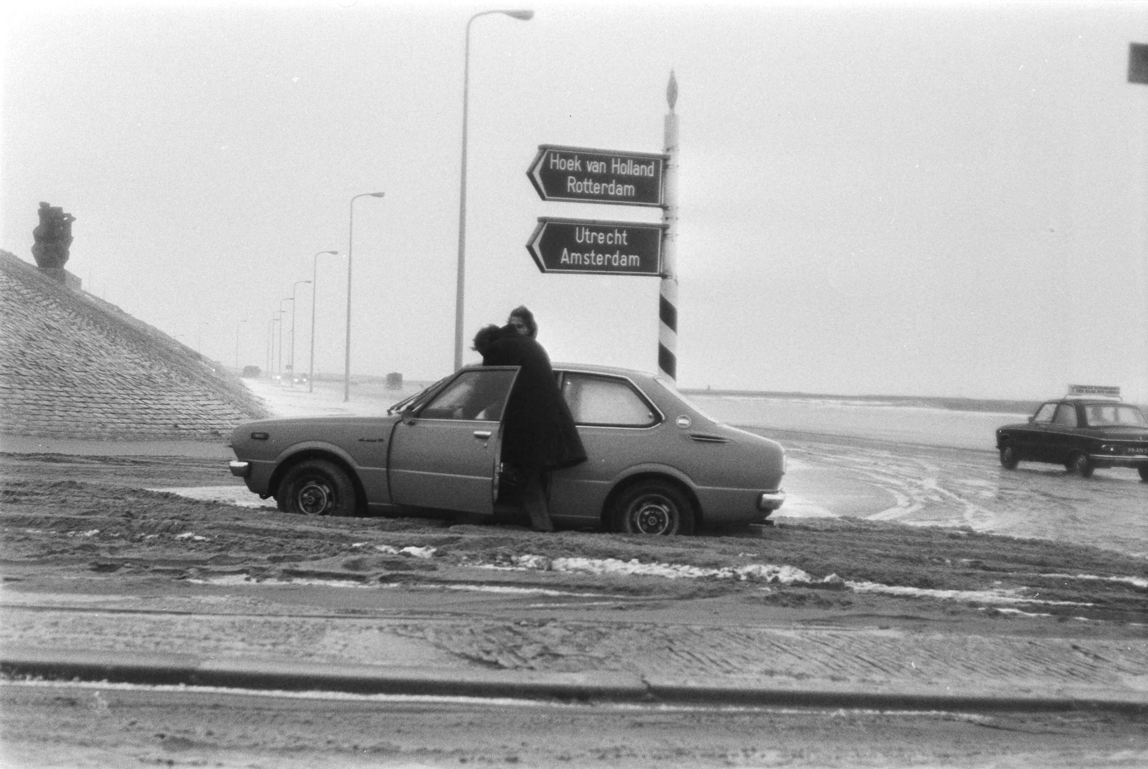 Fotocollectie Anefo — Opgewaaid zand op Scheveningse boulevard met er in vast blijven zitten automobilist die zijn auto duwt — Foto: Peters, Hans / Anefo. Licentie: Set B: Rechtenvrij / Publiek Domein. Bron: Nationaal Archief. http://hdl.handle.net/10648/aca97c2a-d0b4-102d-bcf8-003048976d84