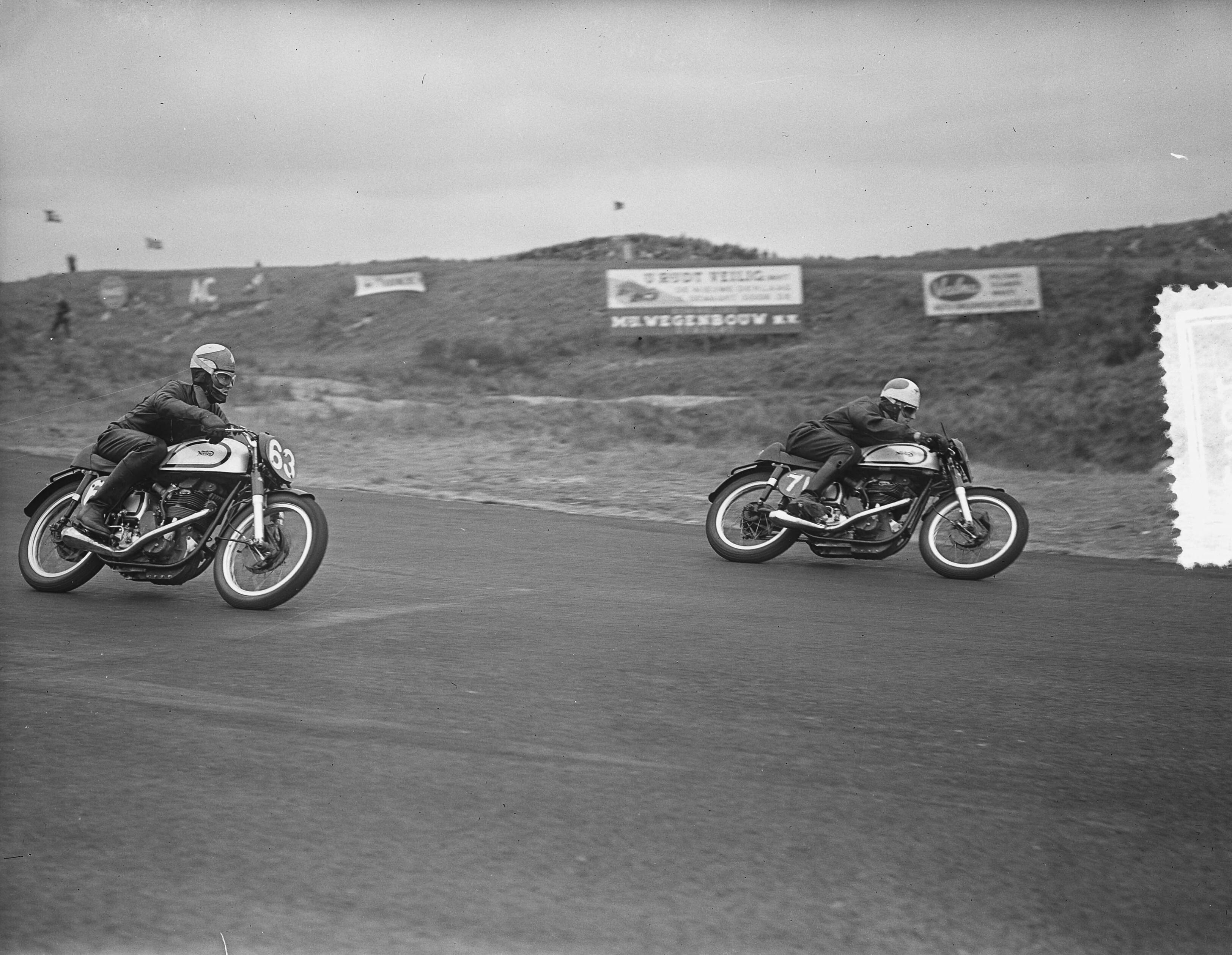 Motorraces Zandvoort — Motorraces op het circuit van Zandvoort. 350cc klasse. Met nummer 71 Piet Bakker, die als 2e zou eindigen. Met nummer 63 de latere winnaar, de Australiër Jack Ahearn — Foto: Bilsen, Joop van / Anefo. Licentie: Set B: Rechtenvrij / Publiek Domein. Bron: Nationaal Archief. http://hdl.handle.net/10648/a922073e-d0b4-102d-bcf8-003048976d84