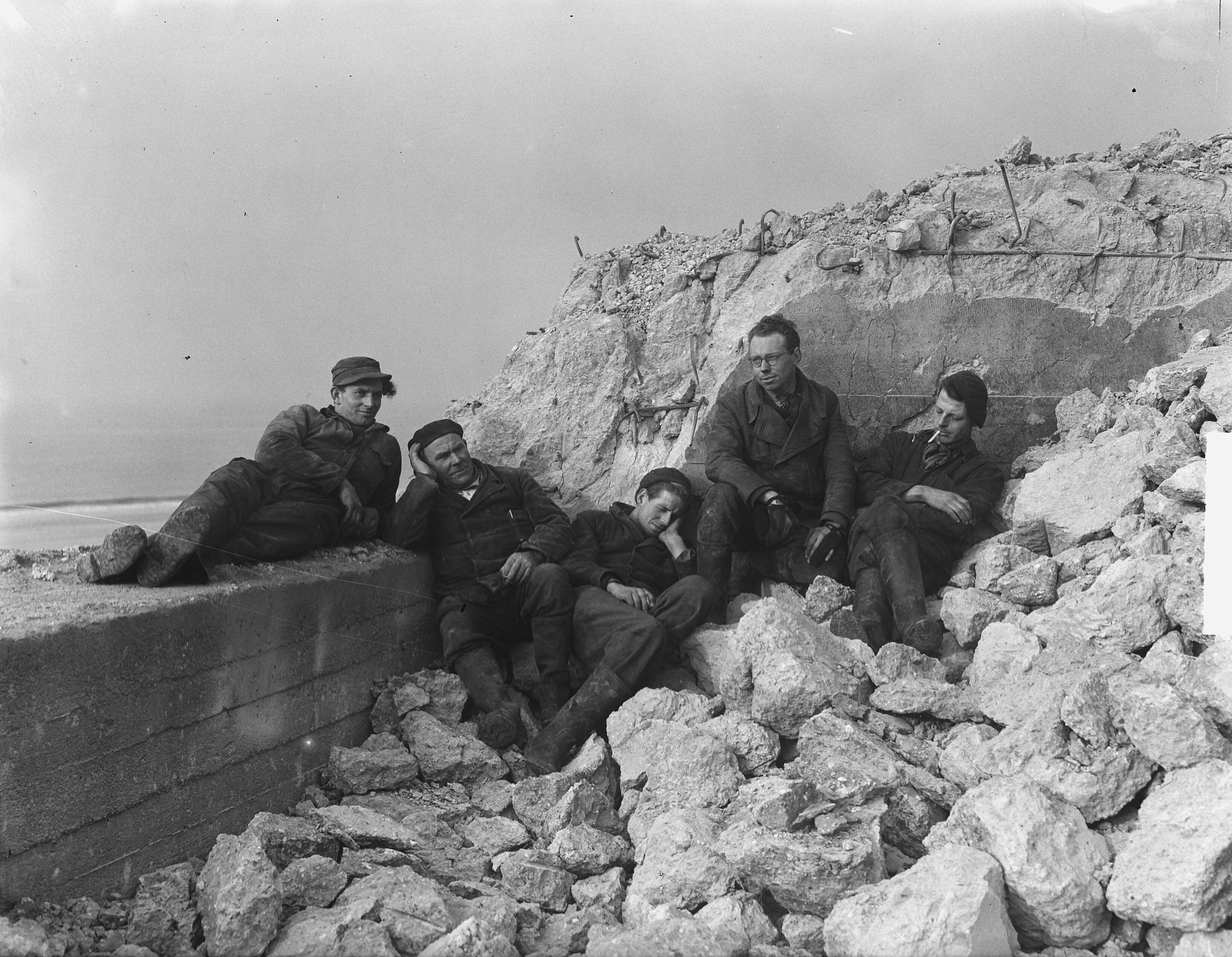 Arbeiders pauzeren in de zon tijdens de sloop van bunkers te Zandvoort — Foto: Vogel, Carel L. de / Anefo. — Licentie: Set B: Rechtenvrij / Publiek Domein. Bron: Nationaal Archief. http://hdl.handle.net/10648/a8e5be82-d0b4-102d-bcf8-003048976d84