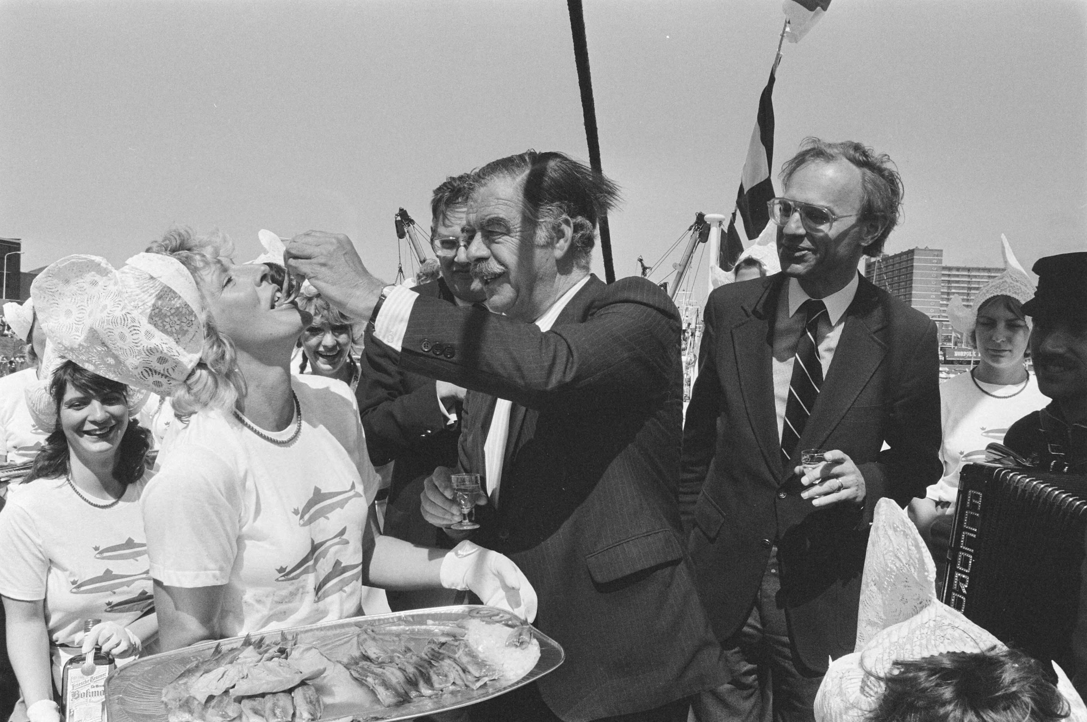 Fotocollectie Anefo — Traditionele Vlaggetjesdag in Scheveningen aan begin haringvangst; minister van Aardenne, Ploeg en min. Ruding bij haringmeisje — Foto: Croes, Rob C. / Anefo. Licentie: Set B: Rechtenvrij / Publiek Domein. Bron: Nationaal Archief. http://hdl.handle.net/10648/ad5398d6-d0b4-102d-bcf8-003048976d84