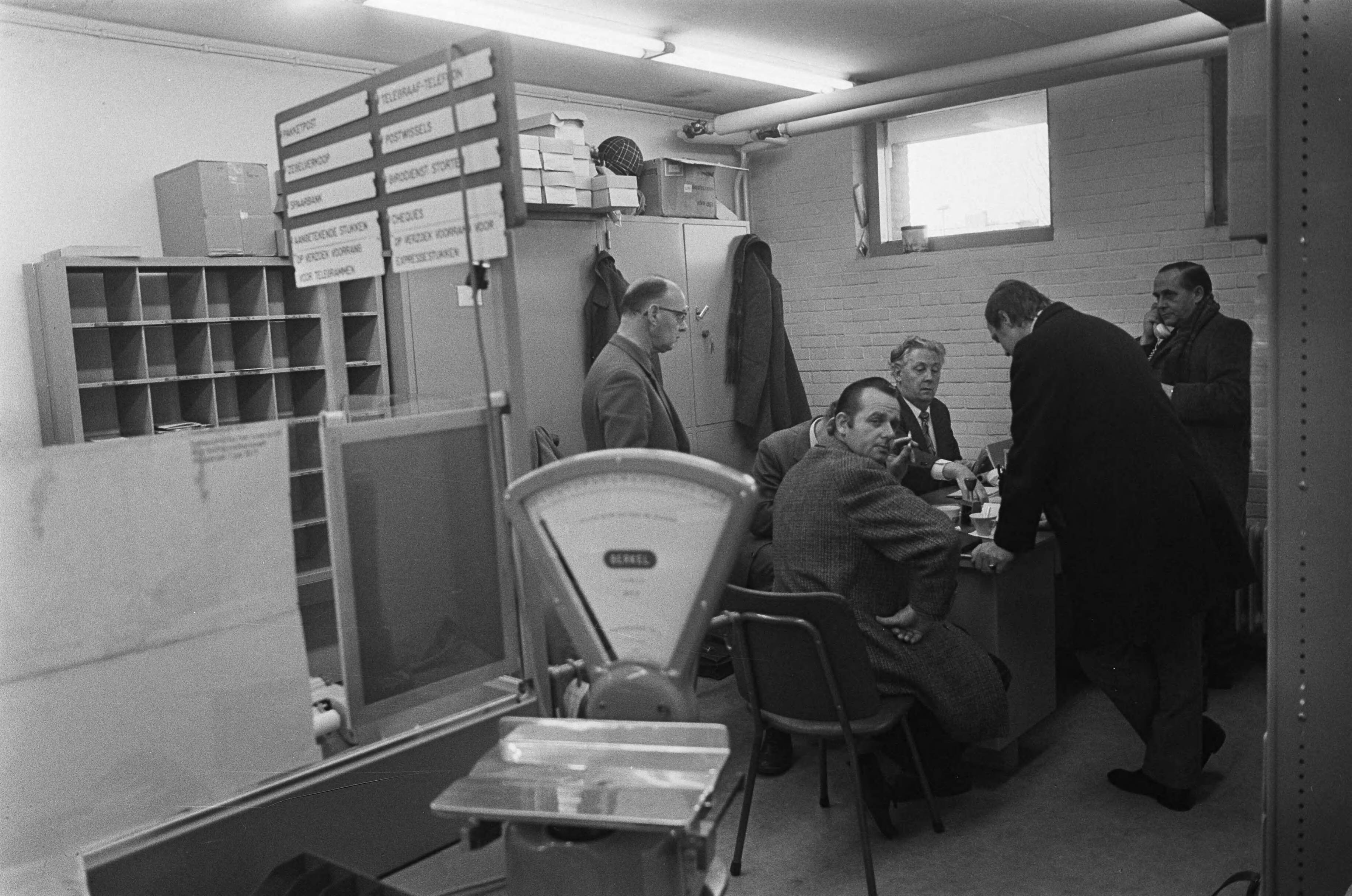 Fotocollectie Anefo — Overval op postagentschap in Haarlemse wijk Schalkwijk, politiemensen in het agentschap — Foto: Peters, Hans / Anefo. Licentie: Set B: Rechtenvrij / Publiek Domein. Bron: Nationaal Archief. http://hdl.handle.net/10648/ac23cf1c-d0b4-102d-bcf8-003048976d84