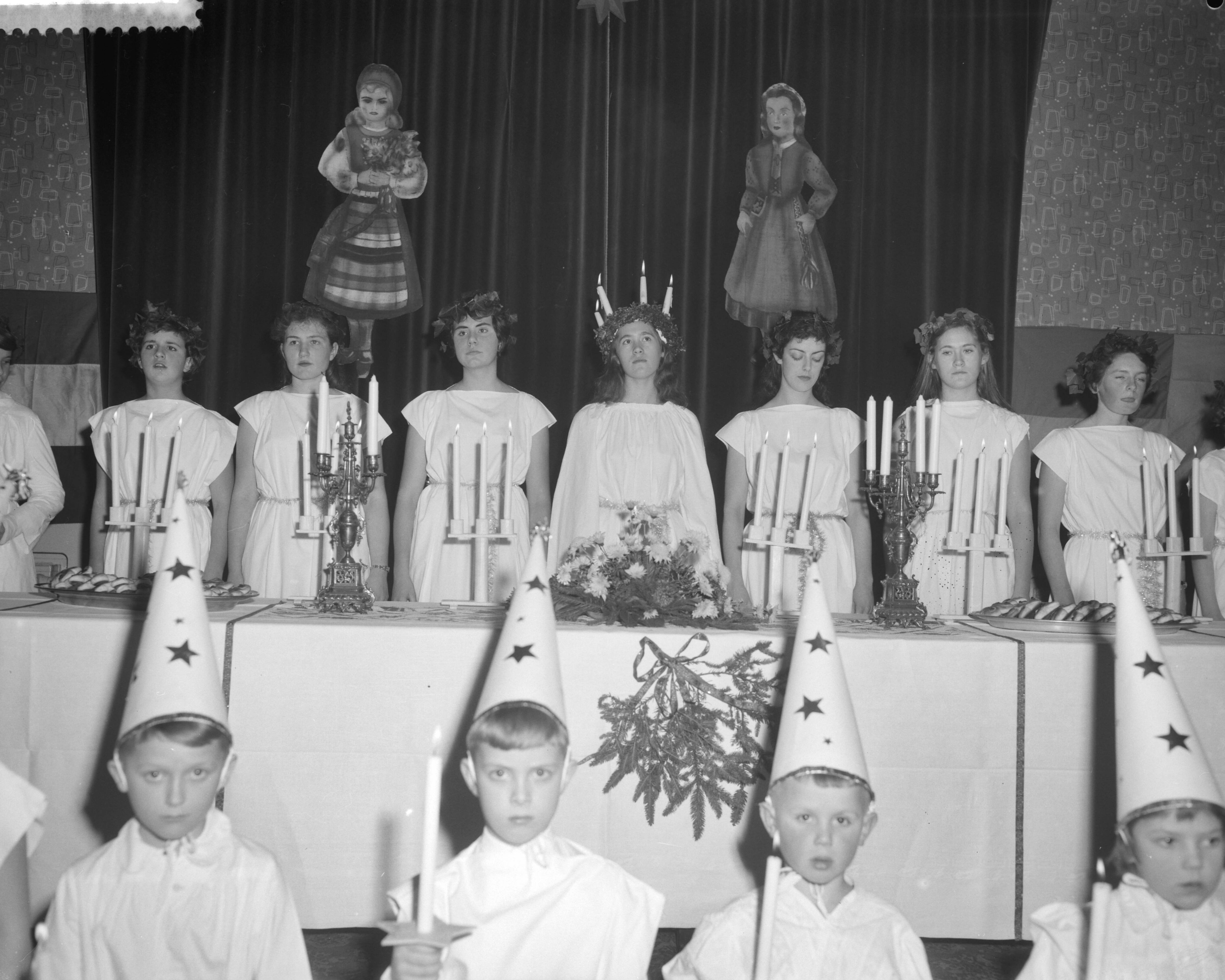 Fotocollectie Anefo — Viering van het Luciafeest door de Zweeds Nederlandse Vereniging in de Dierentuin te Den Haag , in het midden Lucia, de 18-jarige Helbertijn Küller uit Den Haag geflankeerd door de "ternin"(dienstmaagden). Voor haar de "sterrejongens" — Foto: Behrens, Herbert F. / Anefo. Licentie: Set B: Rechtenvrij / Publiek Domein. Bron: Nationaal Archief. http://hdl.handle.net/10648/a9a3ad3e-d0b4-102d-bcf8-003048976d84