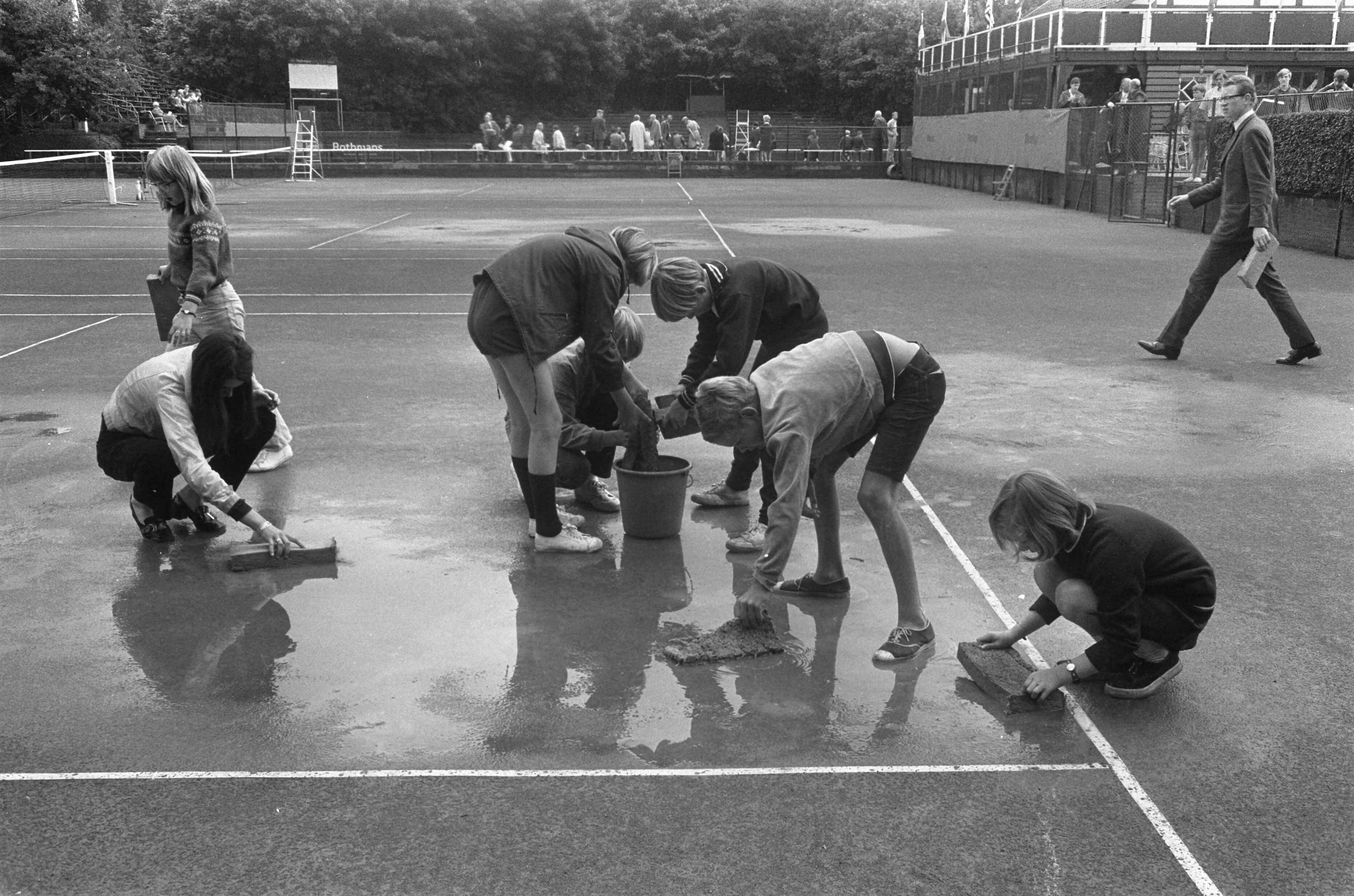 Fotocollectie Anefo — Internationale tenniskampioenschappen te Hilversum ( t Melkhuisje ); de baan wordt droog gemaakt — Foto: Koch, Eric / Anefo. Licentie: Set B: Rechtenvrij / Publiek Domein. Bron: Nationaal Archief. http://hdl.handle.net/10648/ab9df662-d0b4-102d-bcf8-003048976d84