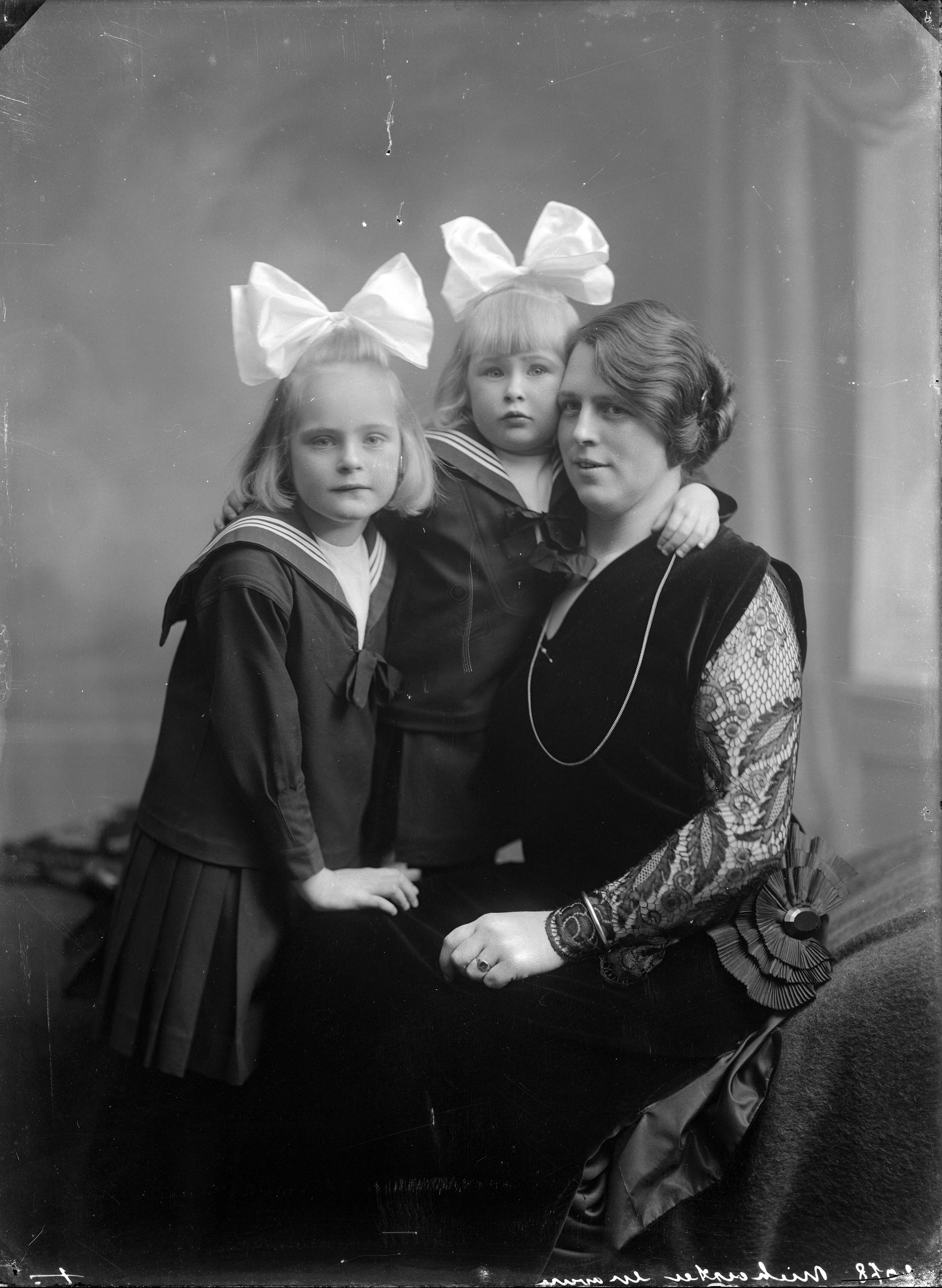 Berg, van den (BERG 050) — Studio-opnames. Een moeder in zwarte jurk met kanten mouwen met haar twee dochters in matrozenpakjes en enorme grote strikken in het blonde haar tegen zich aangeklemd. Haarlem, Nederland. 1918-1930. 2078 Miekeester? gravure — Foto: Berg, Th.C.J. van den / Spaarnestad Photo (05887). Licentie: Set B: Rechtenvrij / Publiek Domein. Bron: Nationaal Archief. http://hdl.handle.net/10648/35429da7-c70f-a382-e063-6df0900a6686