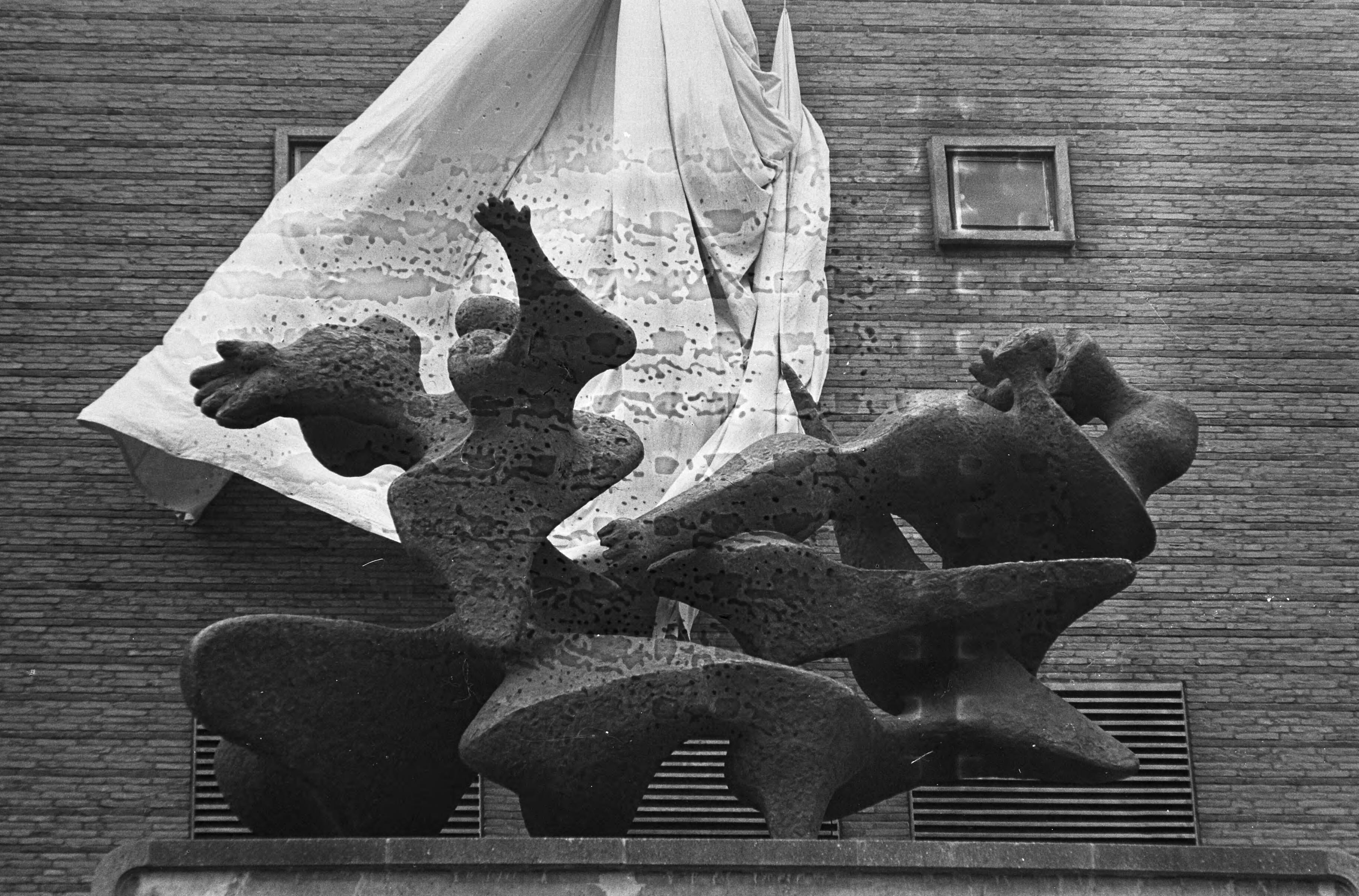 Fotocollectie Anefo — Bronsplastiek "Jacob en de Engel" van de Amsterdamse beeldhouwer C. Kneulman op de luifel van het politiebureau in Den Haag onthuld door burgemeester mr. H.A.M.T. Kolfschoten. Het doek wordt opgetrokken en het beeld wordt zichtbaar op 20m hoogte — Foto: Koch, Eric / Anefo. Licentie: Set B: Rechtenvrij / Publiek Domein. Bron: Nationaal Archief. http://hdl.handle.net/10648/aa4528e4-d0b4-102d-bcf8-003048976d84