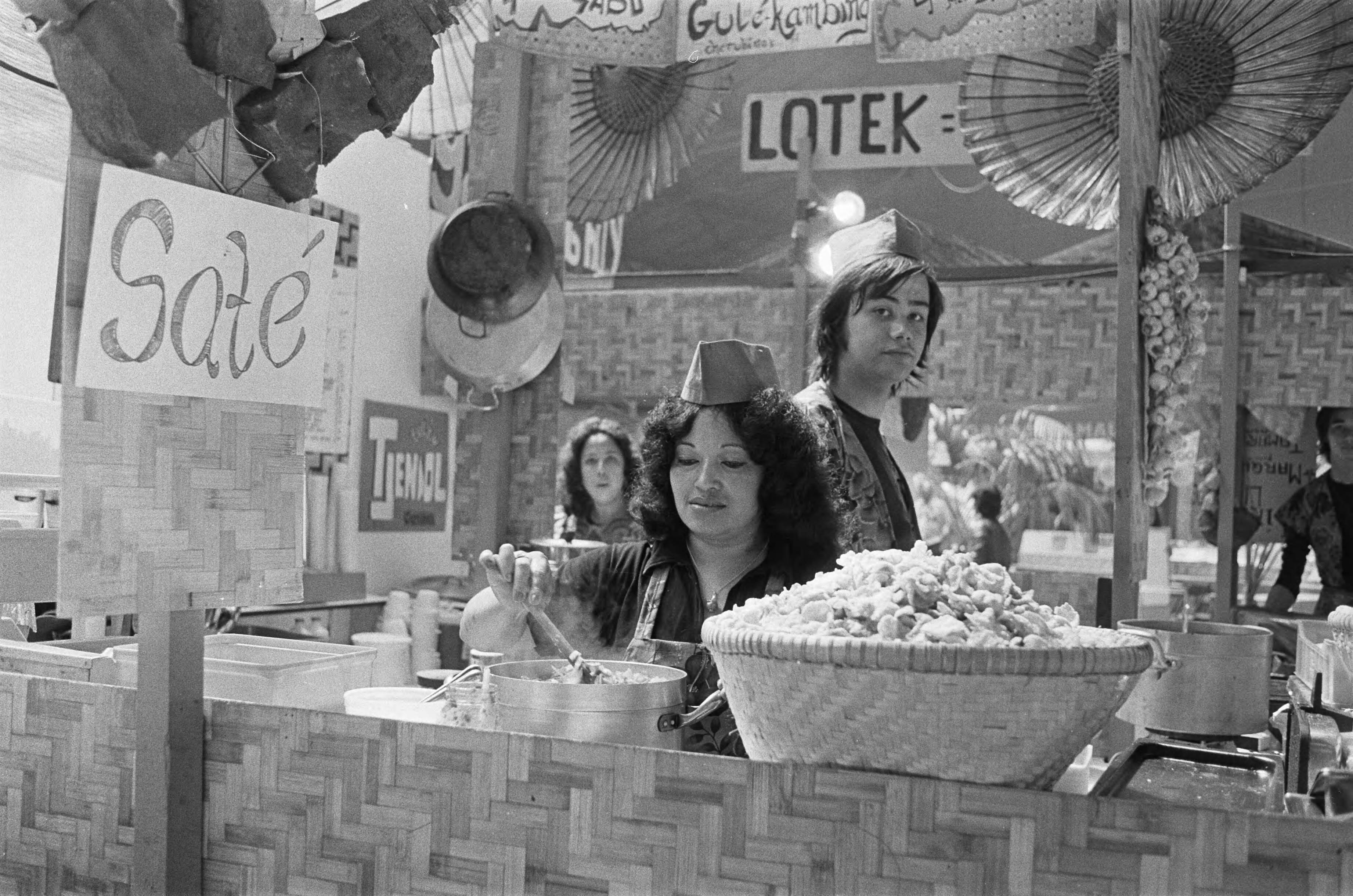 Pasar Malam in de Houtrusthallen in Den Haag — Stand met etenswaren op de Pasar Malam — Foto: Bogaerts, Rob / Anefo. Licentie: Set B: Rechtenvrij / Publiek Domein. Bron: Nationaal Archief. http://hdl.handle.net/10648/ac6be982-d0b4-102d-bcf8-003048976d84
