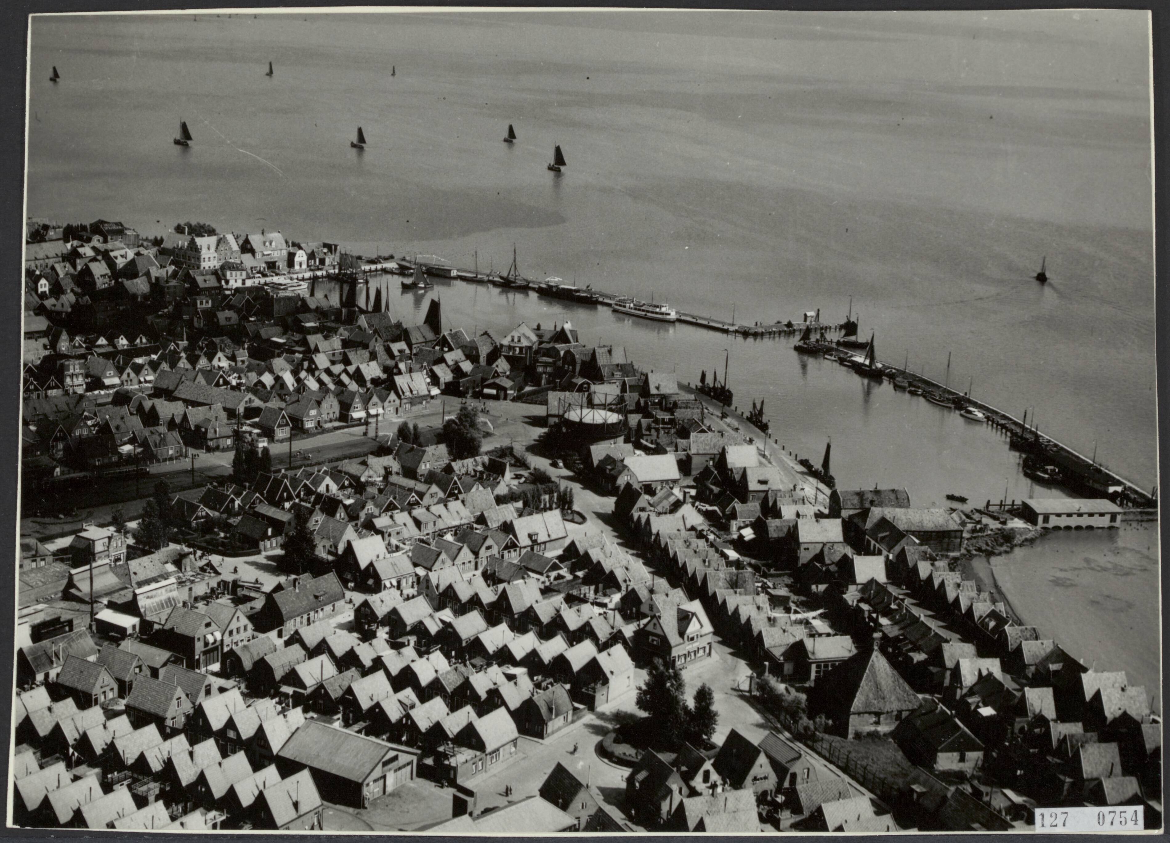Fotocollectie Rijksvoorlichtingsdienst Eigen — Luchtopname. Volendam bezit een geheel kunstmatige haven. Buien de zeedijk omsluiten twee dammen een bassin dat een ligplaats biedt aan d vele vissersvaartuigen — Foto: Aerophoto "Nederland" / Rechtenvrij. Licentie: Set B: Rechtenvrij / Publiek Domein. Bron: Nationaal Archief. http://hdl.handle.net/10648/af3f8d1c-d0b4-102d-bcf8-003048976d84