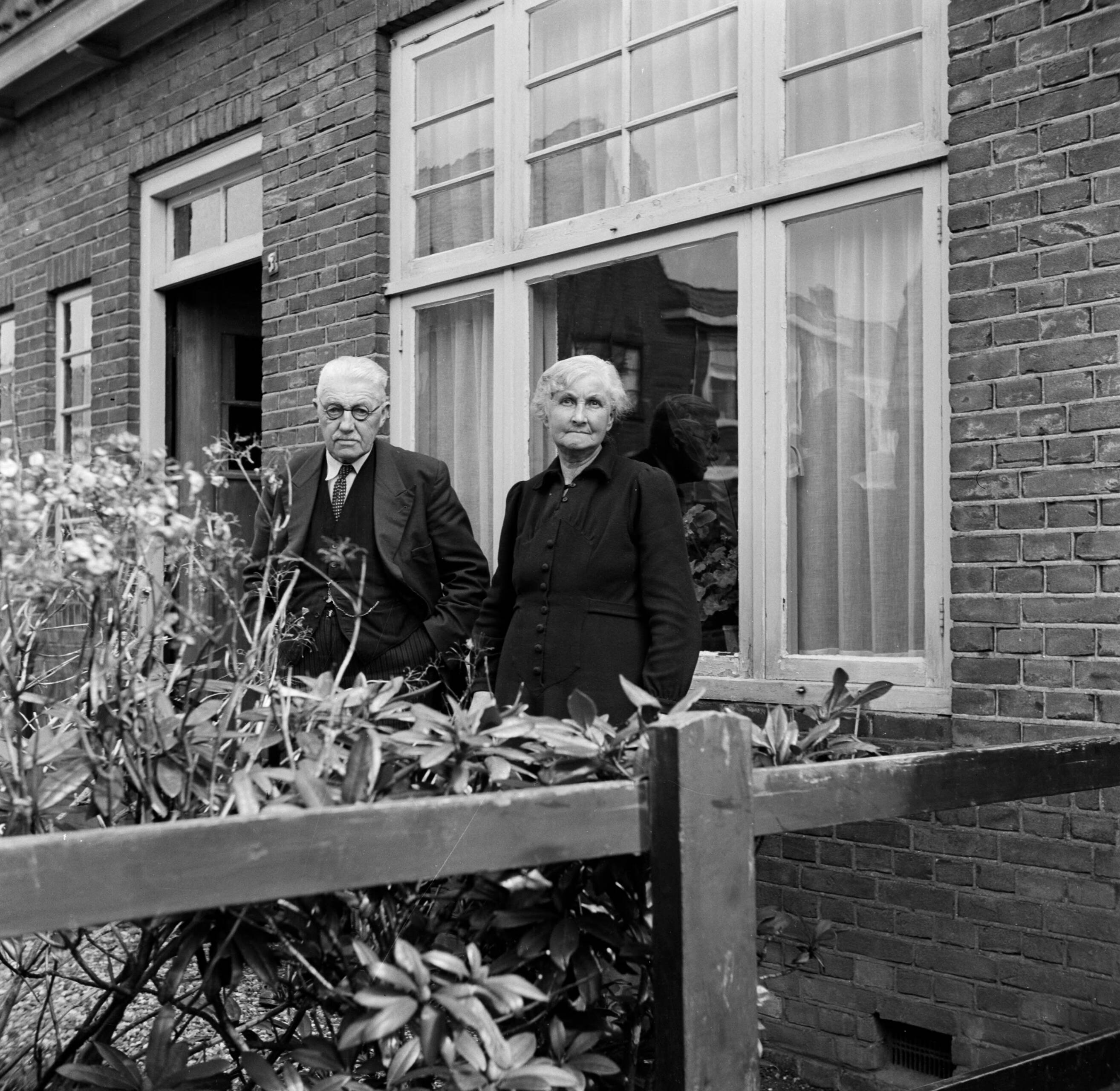 Fotocollectie Van de Poll — Het echtpaar S. de Jong in de tuin voor hun woning in het Friese Huizum (nu deel van Leeuwarden) — Foto: Poll, Willem van de. Licentie: Set B: Rechtenvrij / Publiek Domein. Bron: Nationaal Archief. http://hdl.handle.net/10648/aeccc2d2-d0b4-102d-bcf8-003048976d84