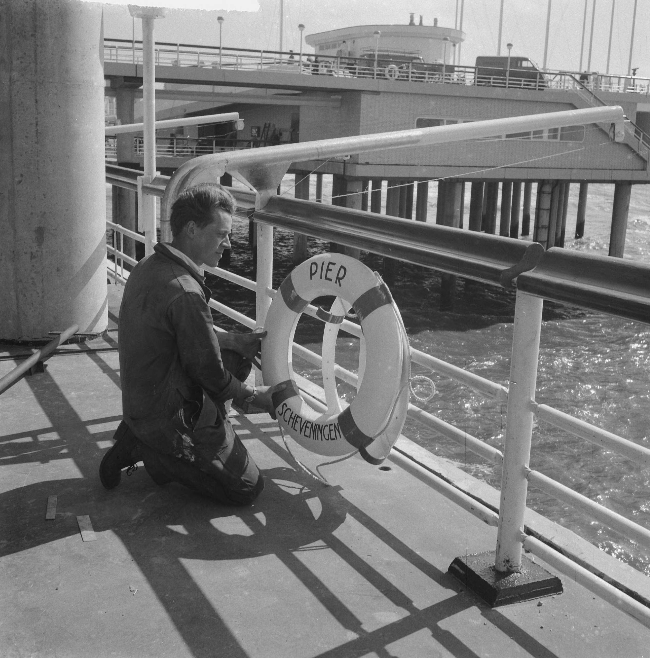 Nieuwe Pier in Scheveningen — Nieuwe Pier in Scheveningen. Arbeider bevestigt reddingsboei — Foto: Nijs, Jac. de / Anefo. Licentie: Set B: Rechtenvrij / Publiek Domein. Bron: Nationaal Archief. http://hdl.handle.net/10648/a9d5afd2-d0b4-102d-bcf8-003048976d84