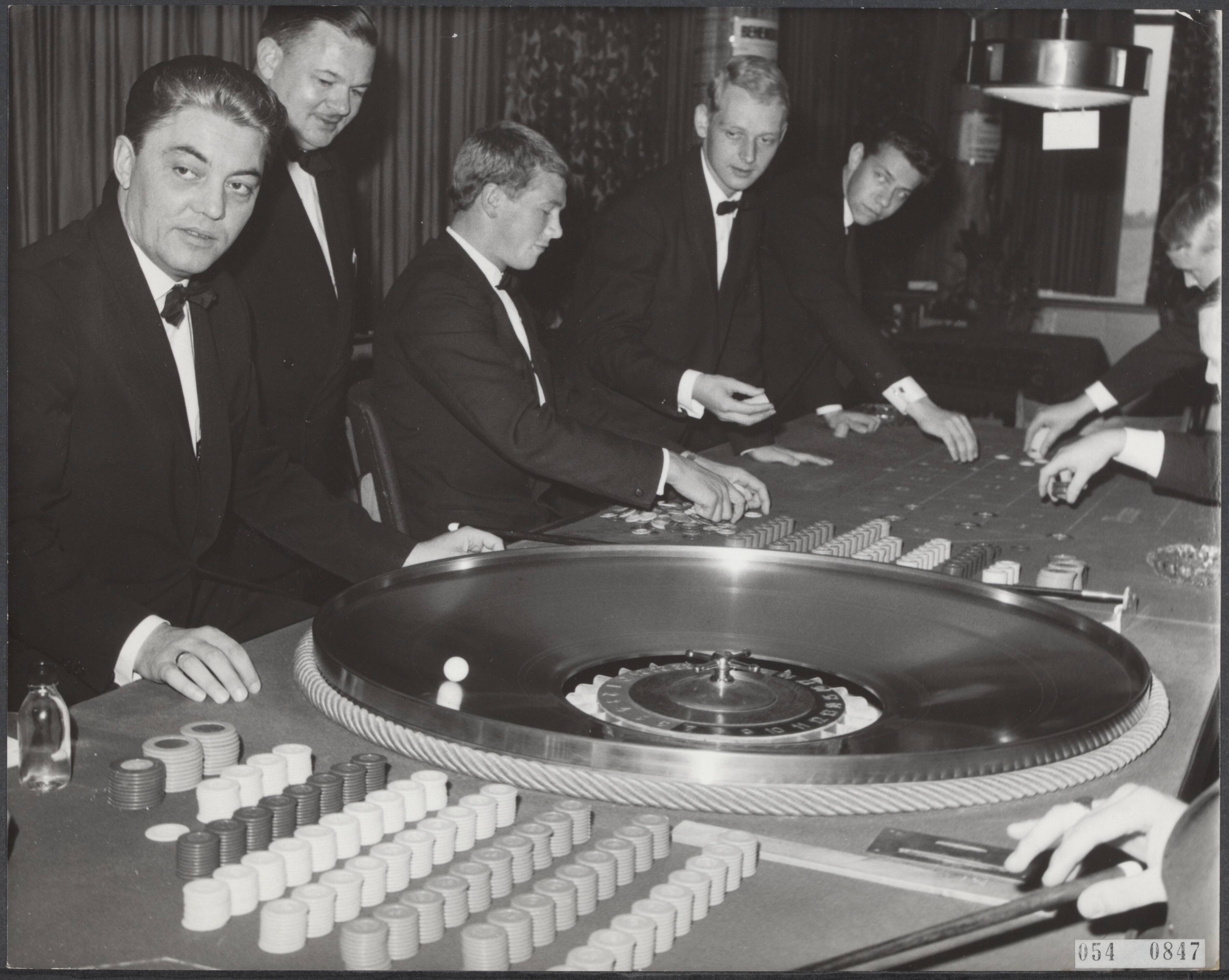 Fotocollectie Elsevier Binnenland — Laatste dag dat in Nederland gespeeld kan worden in de casino's, de minister van Justitie heeft met ingang van 22 oktober 1965 de zogenaamde behendigheidsspelen verboden. In Casino West-End te Loosdrecht (5000 leden) wordt voor het laatst het spel Delphi 24 gespeeld — Foto: Evers, Joost / Anefo. Licentie: Set B: Rechtenvrij / Publiek Domein. Bron: Nationaal Archief. http://hdl.handle.net/10648/ae07e278-d0b4-102d-bcf8-003048976d84