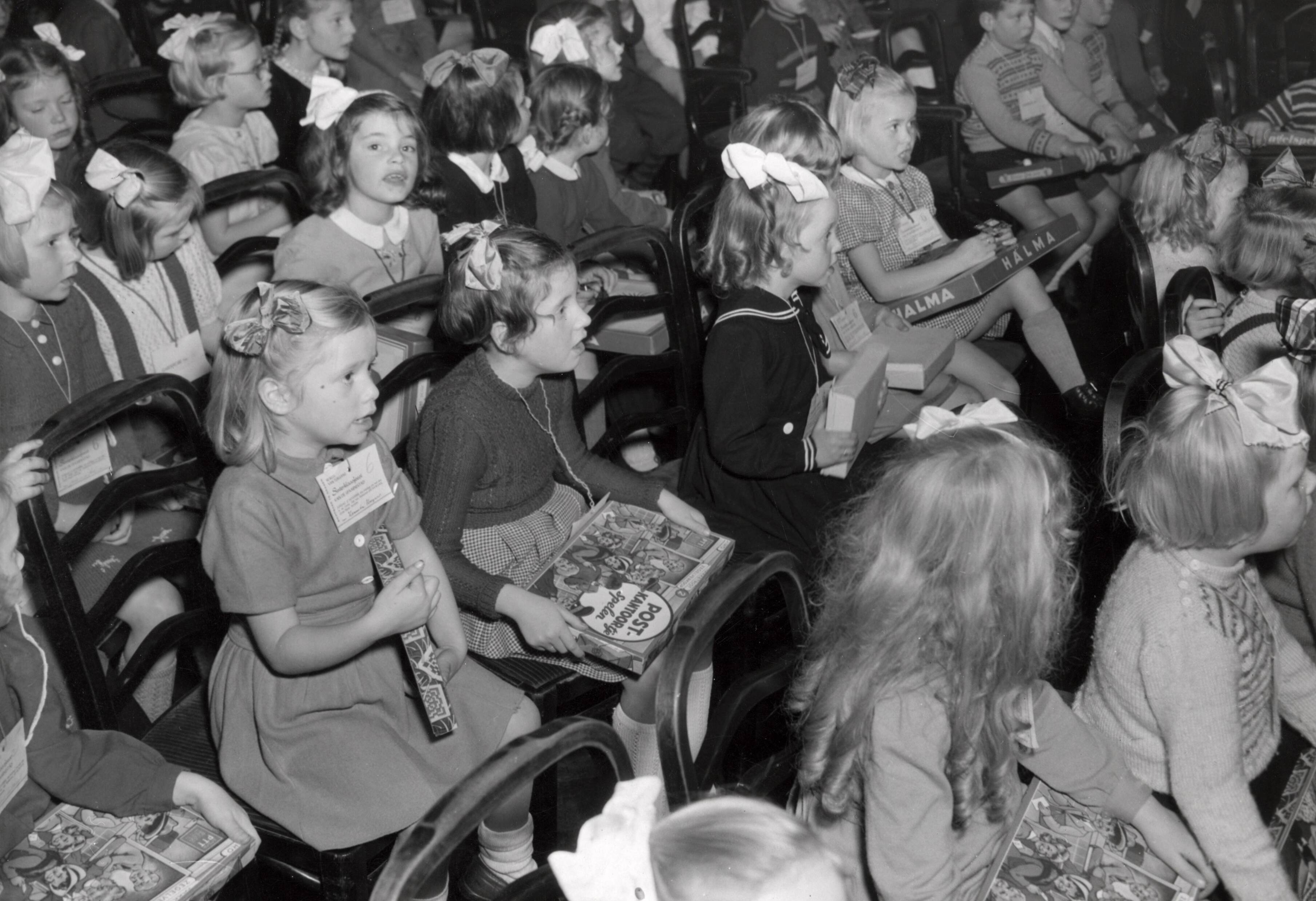 Collectie nader te bepalen — [Sinterklaasfeest N.V. Drukkerij De Spaarnestad in Haarlem] [kinderen in de zaal met op schoot cadeau's — Foto: Fotograaf Onbekend / Fotobureau onbekend / Spaarnestad Photo (05887). Licentie: Set B: Rechtenvrij / Publiek Domein. Bron: Nationaal Archief. http://hdl.handle.net/10648/35429da6-404f-a382-e063-6df0900a6686