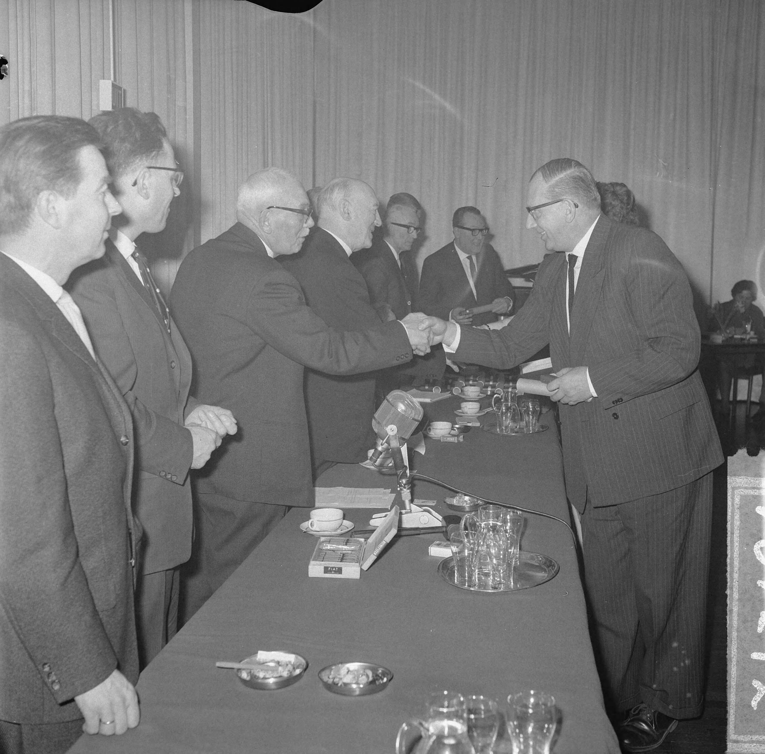 Fotocollectie Anefo — Huldiging in Hotel Gooiland door de NRU van 23 medewerkers die 25 jaar werkzaam zijn bij een van de zuilen, de heer Evers van de KRO gelukgewenst door de voorzitter van de NRU, mr. A.B. Roosjen (links). Naast Roosjen oud-voorzitter prof. Kors — Foto: Gelderen, Hugo van / Anefo. Licentie: Set B: Rechtenvrij / Publiek Domein. Bron: Nationaal Archief. http://hdl.handle.net/10648/aa5c8dae-d0b4-102d-bcf8-003048976d84