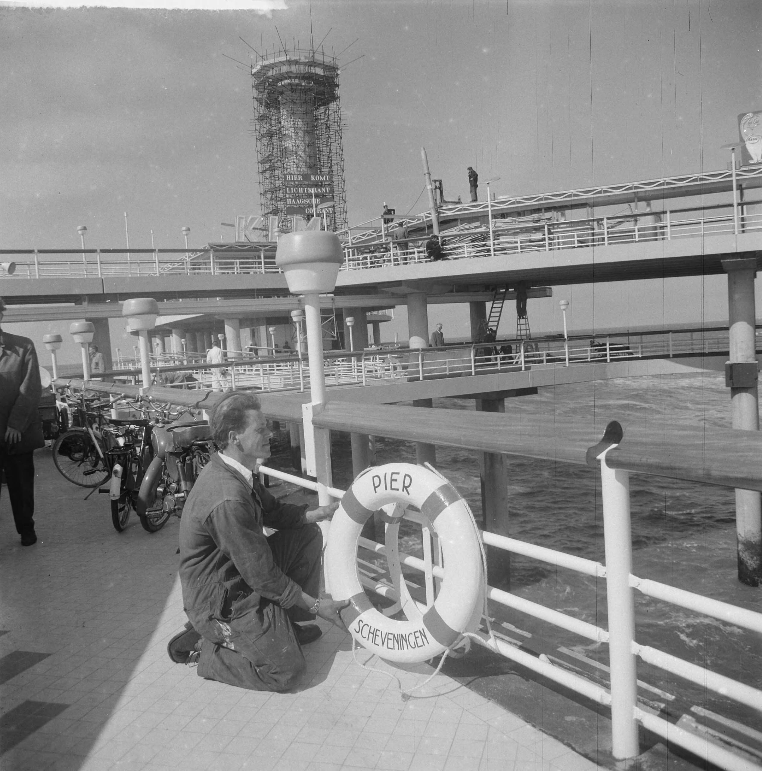 Nieuwe Pier in Scheveningen — Nieuwe Pier in Scheveningen. Arbeider verzorgt de reddingsboeien — Foto: Nijs, Jac. de / Anefo. Licentie: Set B: Rechtenvrij / Publiek Domein. Bron: Nationaal Archief. http://hdl.handle.net/10648/a9d5ace4-d0b4-102d-bcf8-003048976d84