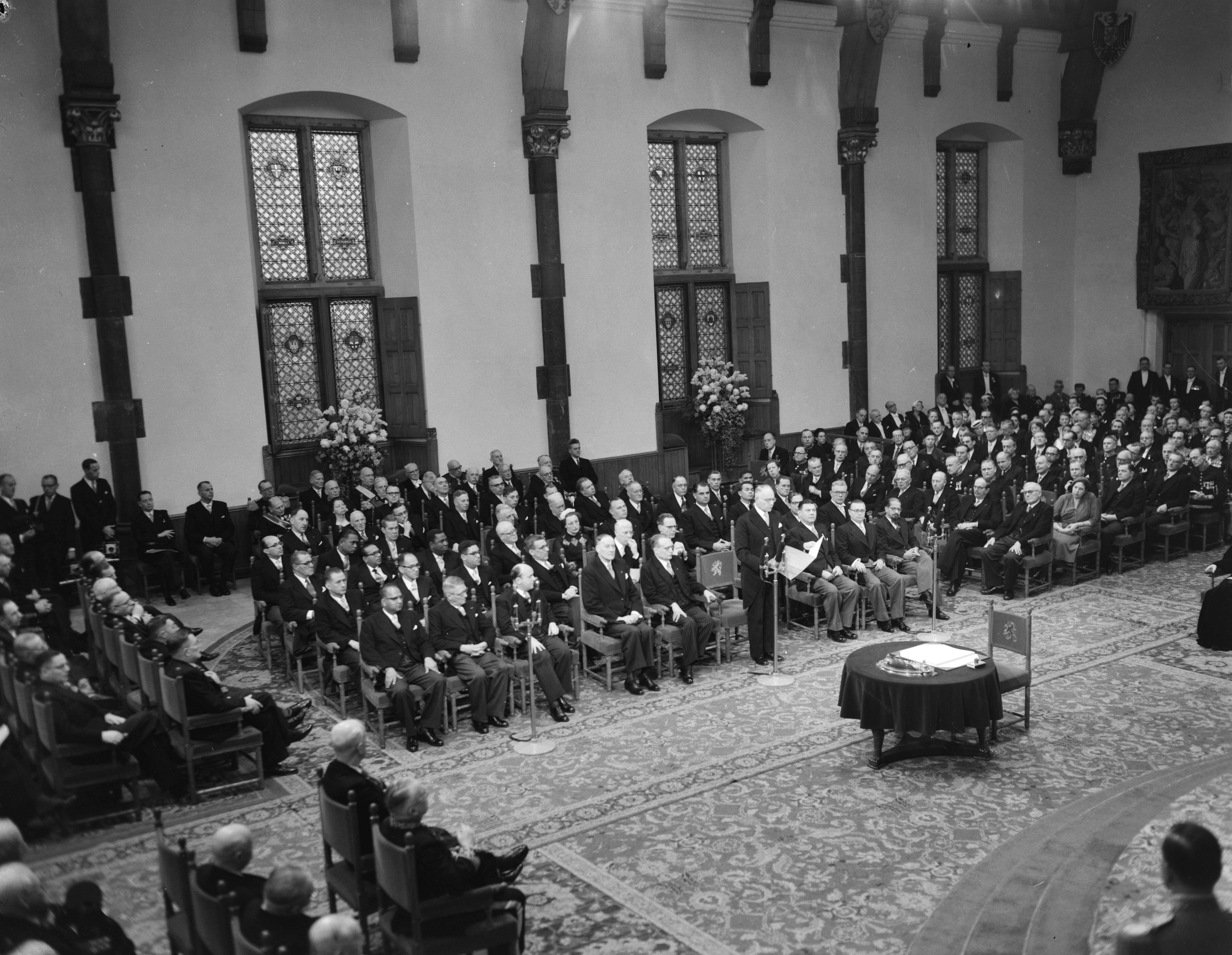 Koningin Juliana ondertekent in een plechtige bijeenkomst in de Ridderzaal in Den Haag de Acte van Bevestiging van het Statuut voor het Koninkrijk — Ondertekening van de Acte van Bevestiging van het Statuut van het Koninkrijk in de Ridderzaal te Den Haag. Één van de ministers houdt een toespraak — Foto: Noske, J.D. / Anefo. Licentie: Set B: Rechtenvrij / Publiek Domein. Bron: Nationaal Archief. http://hdl.handle.net/10648/a92e1b00-d0b4-102d-bcf8-003048976d84